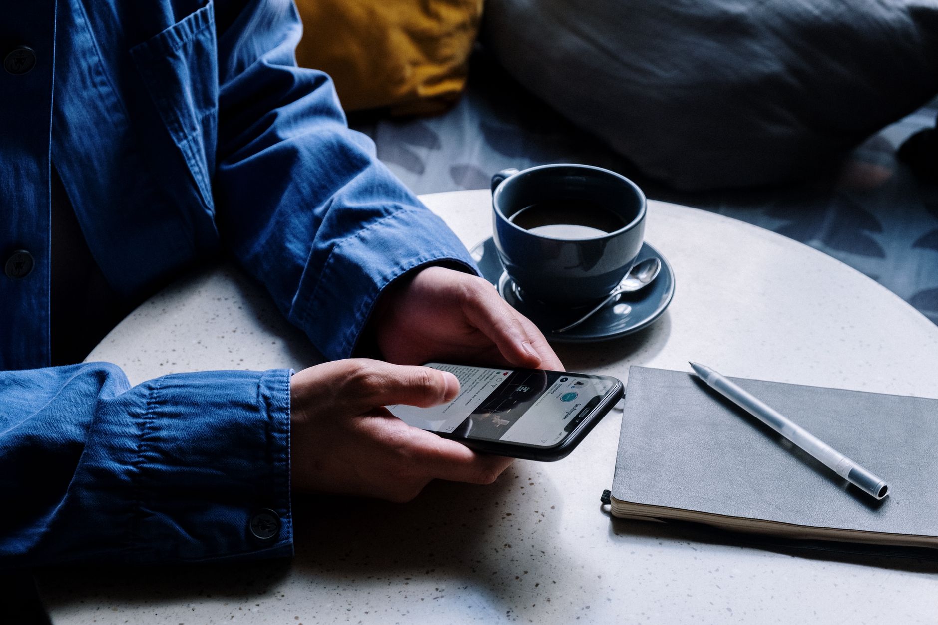 an iPhone screen showing the iCloud settings menu with Hide My Email toggle, resting on a wooden desk beside a cup of coffee