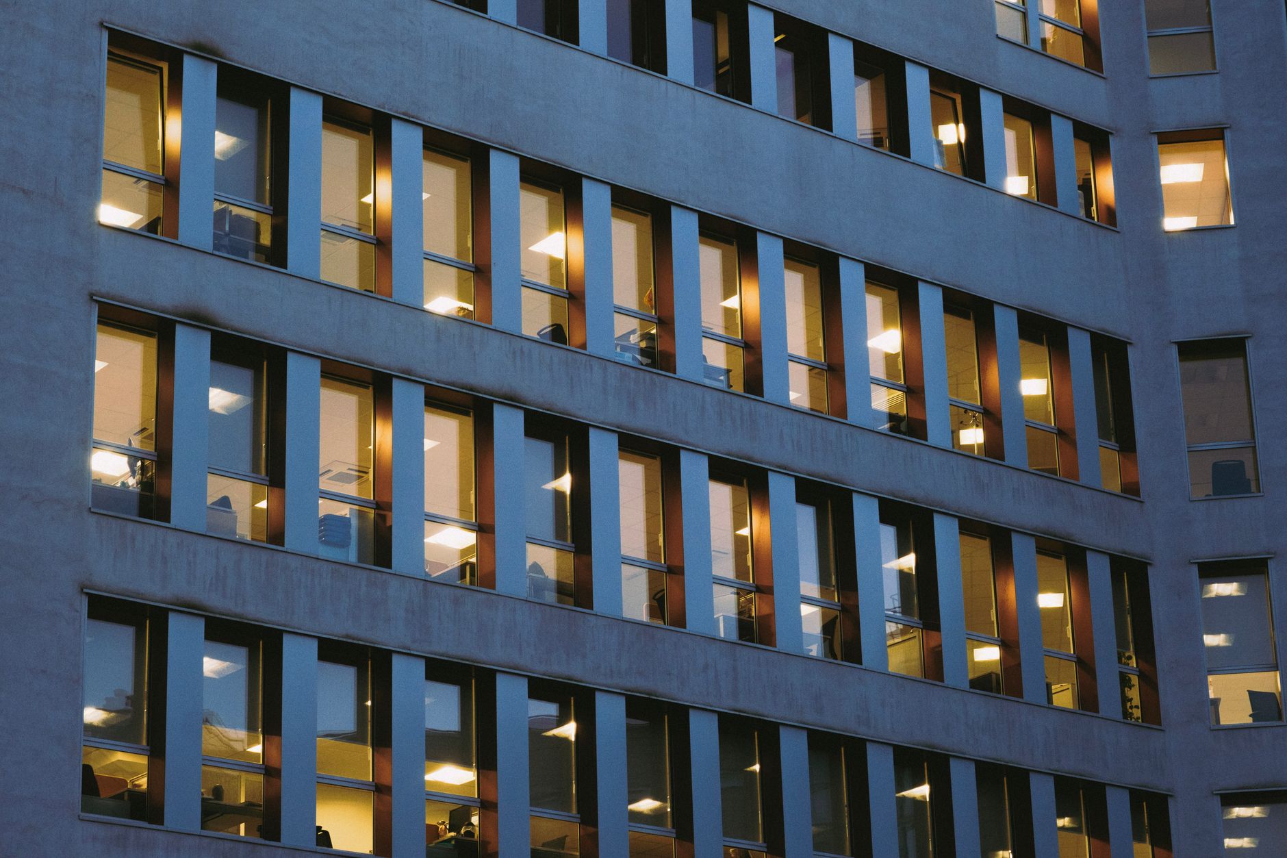 a modern biotech research facility exterior at dusk, glass facade reflecting city lights, with laboratory equipment visible through ground-floor windows