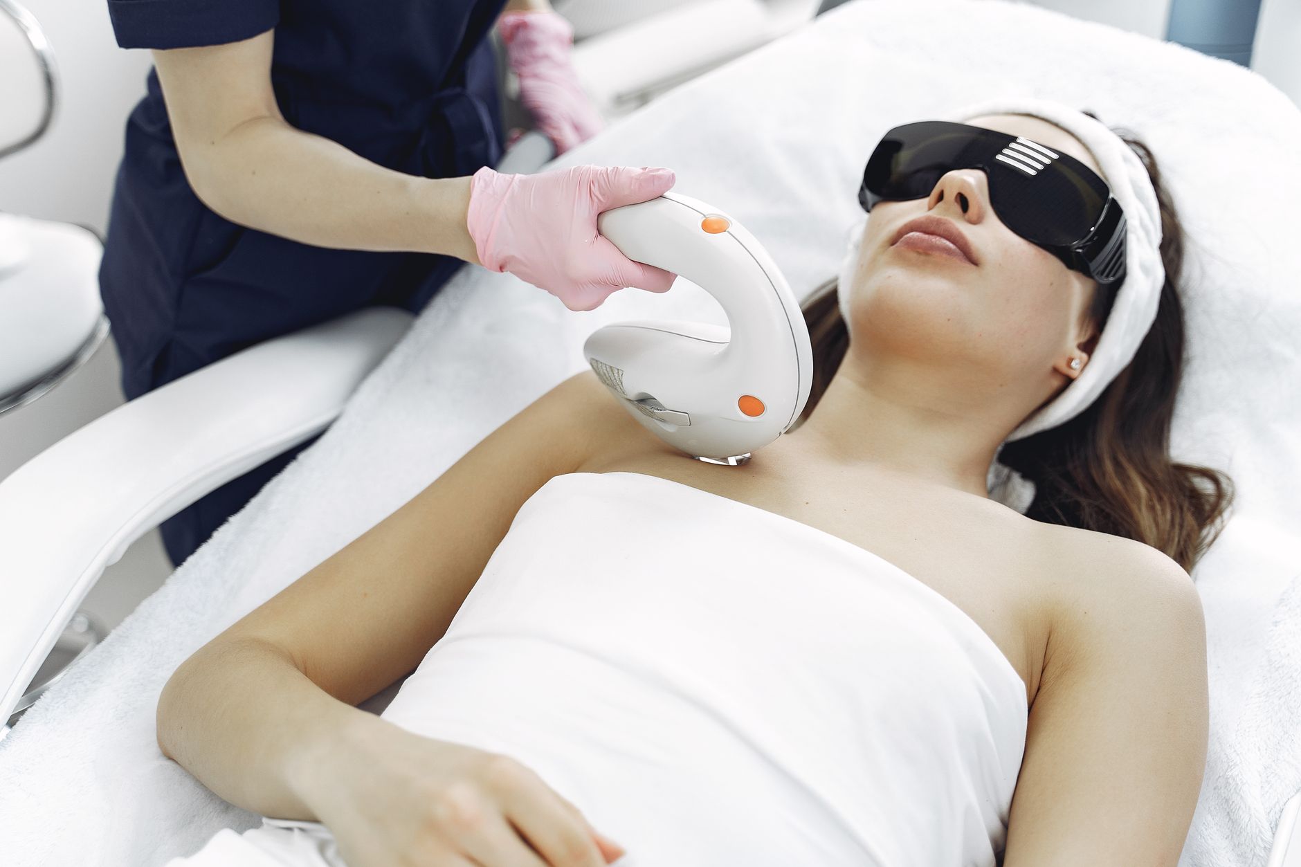 A clinical dermatology treatment room with a laser device positioned above a treatment chair, surrounded by calibration equipment and monitor screens displaying skin imaging data