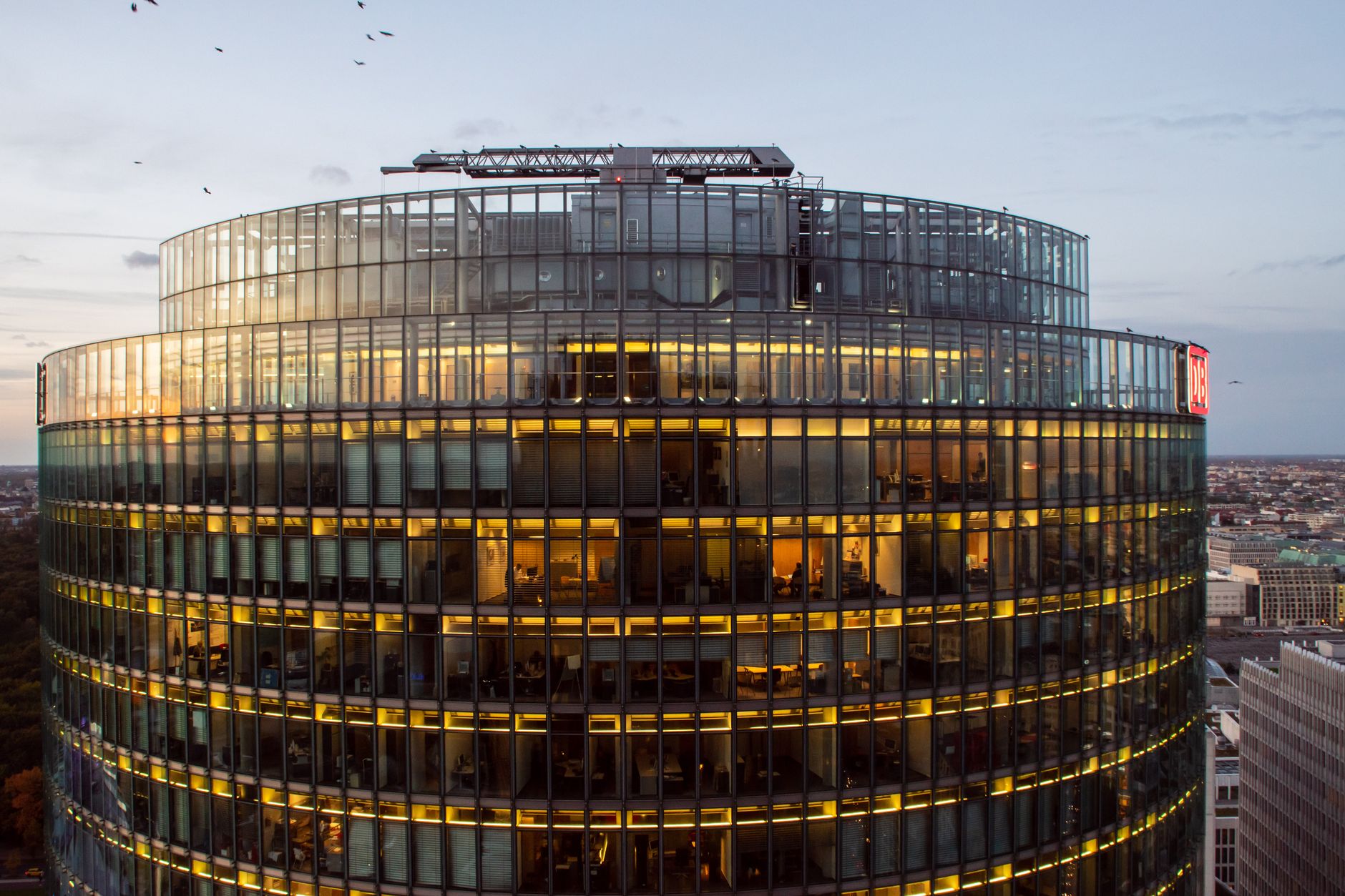 an aerial view of a modern office district at dusk with glass-facade buildings and illuminated windows, set against an urban skyline