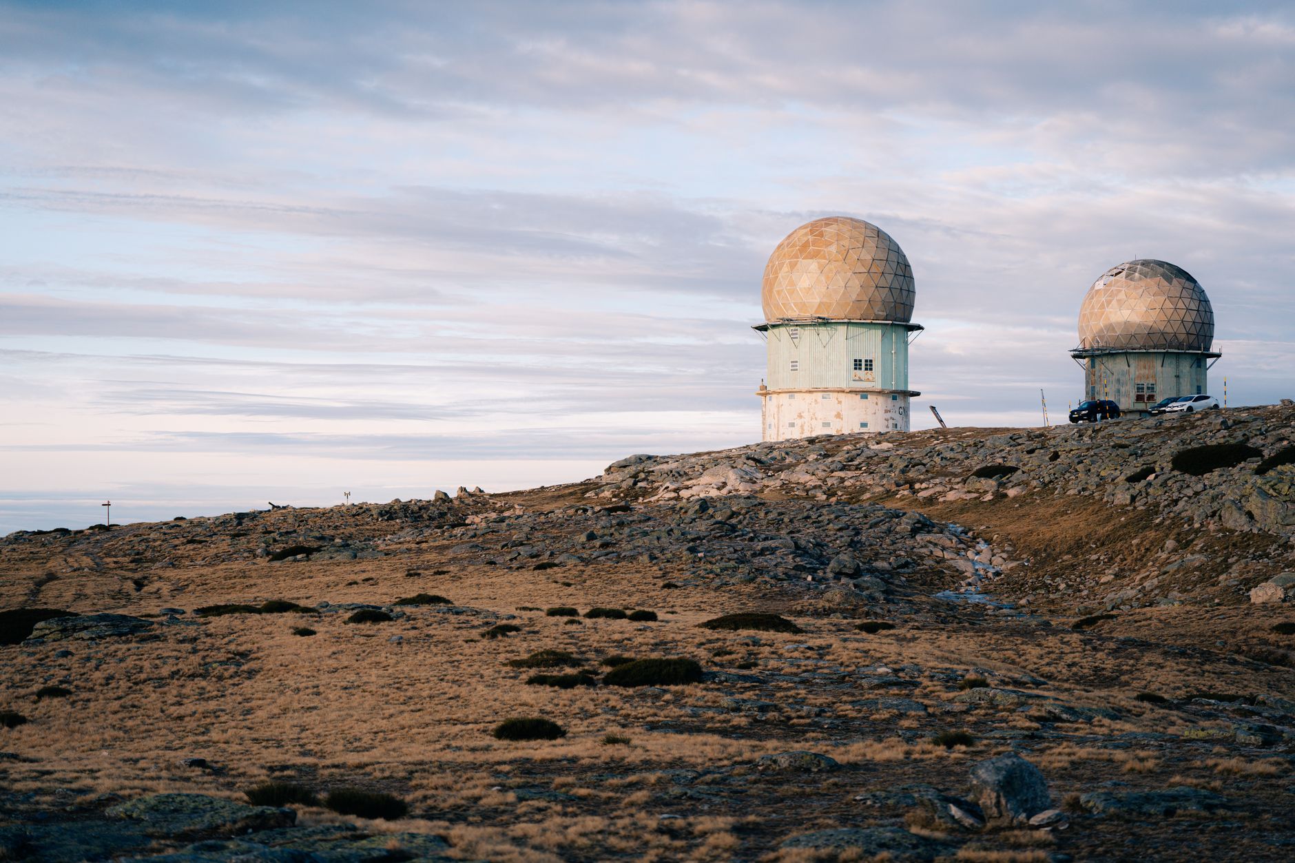 a ground-based missile defense launcher unit positioned on an open hilltop overlooking a coastal landscape at dusk, with radar arrays visible in the background