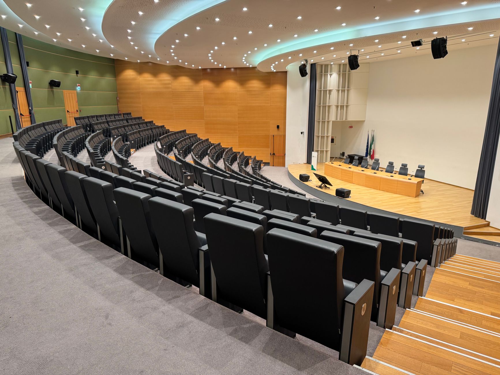 a wide conference hall interior set up for a large engineering society awards ceremony, rows of empty chairs facing a lit stage podium, projection screens flanking the stage