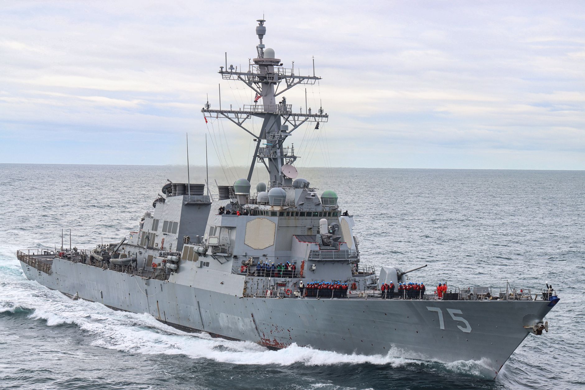 a naval vessel at sea with a missile defense radar array mounted on its deck, photographed at dusk against an open ocean horizon