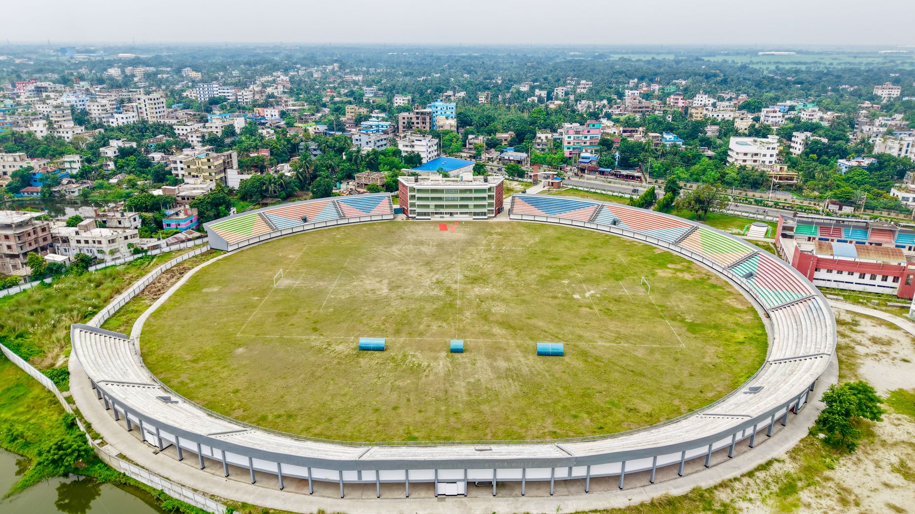 aerial view of a large open football stadium under intense midday sun with a hazy, dust-filtered sky visible above the pitch
