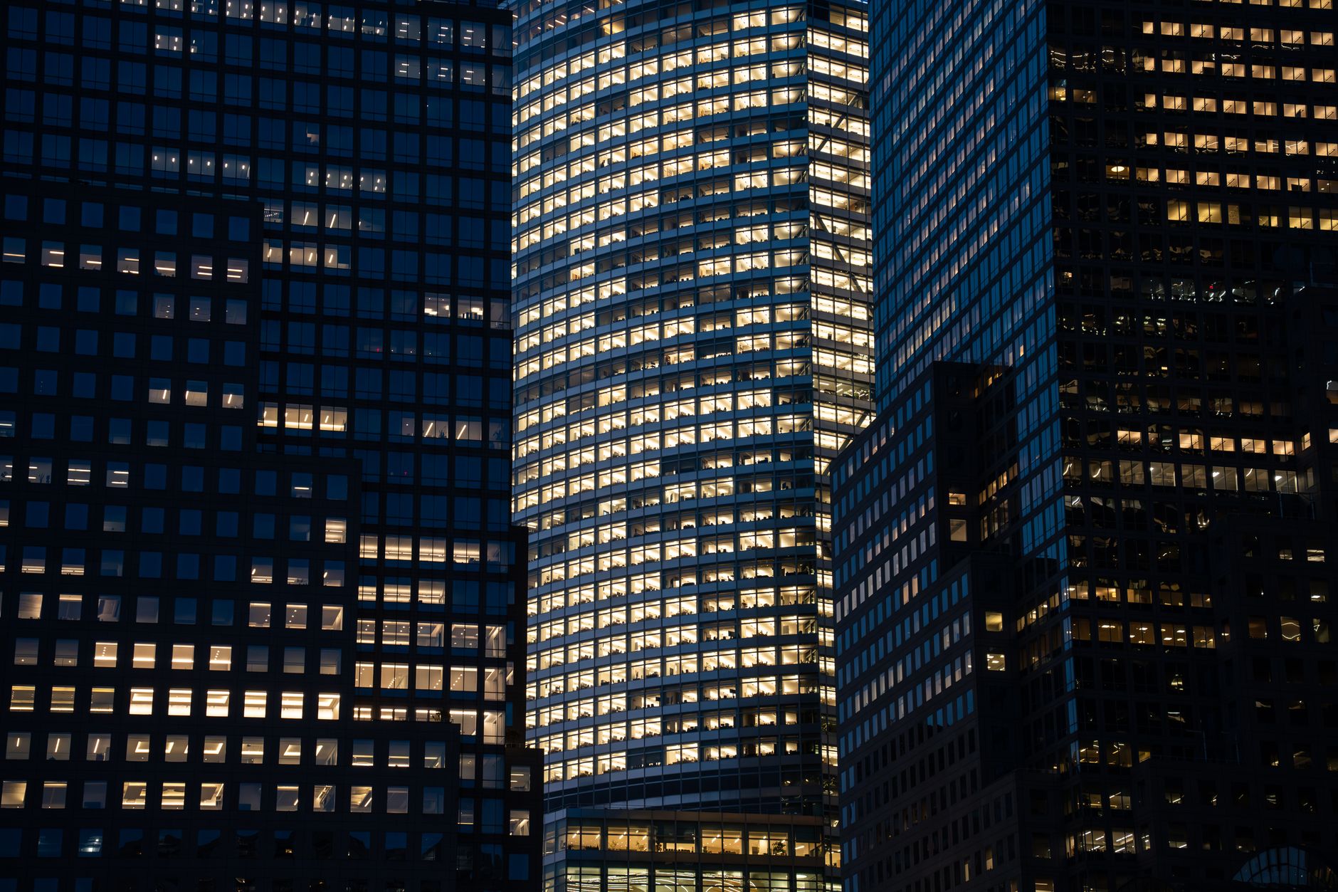 a wide-angle view of a modern financial district skyline at dusk, with illuminated office tower windows reflected in a glass facade