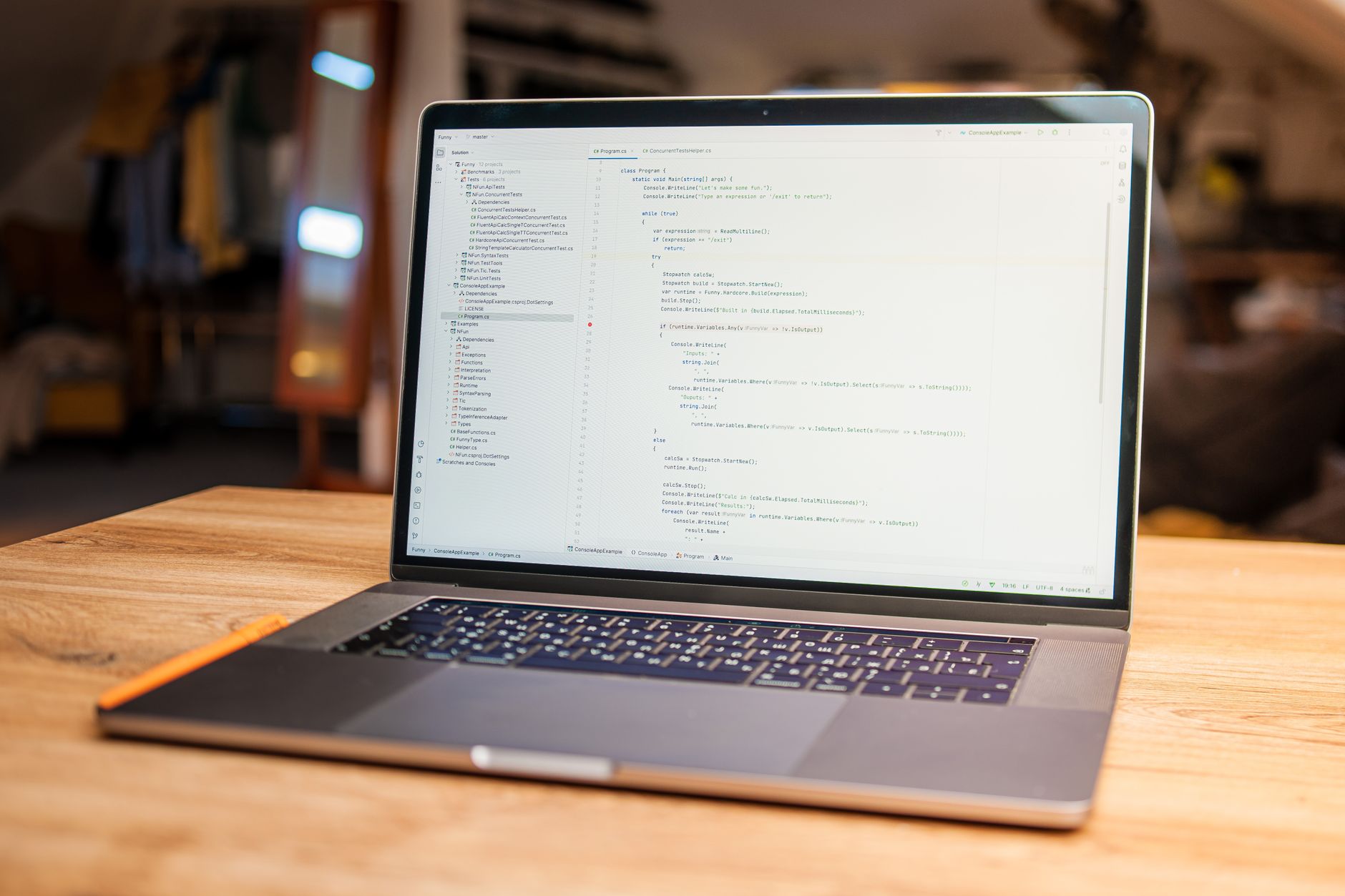 a MacBook laptop open on a wooden desk displaying a dark-themed terminal and code editor interface, with an external microphone positioned beside it