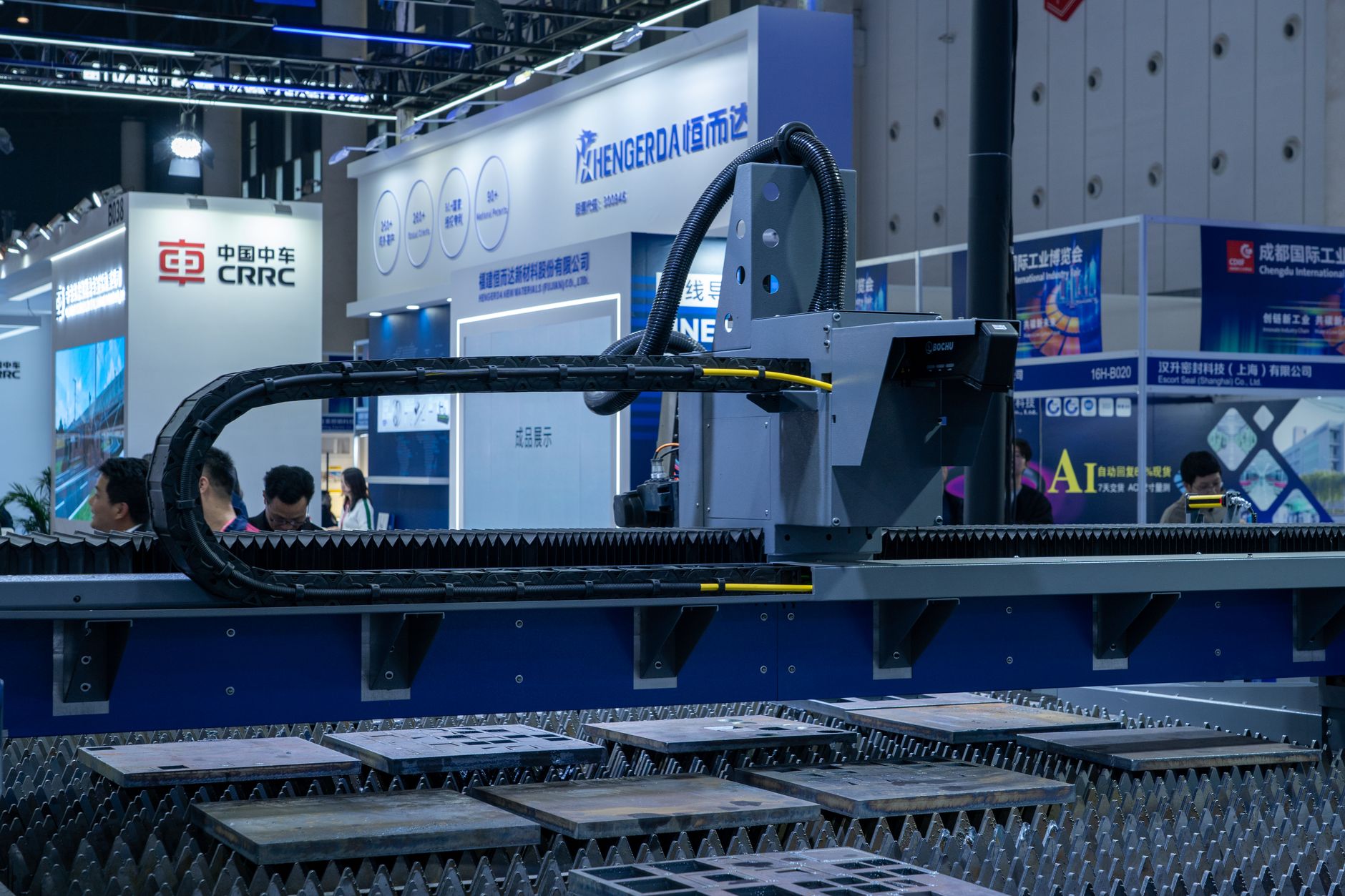 wide-angle view of a large convention center exhibition hall filled with interactive display screens and hardware demonstration stations, captured from an elevated mezzanine level