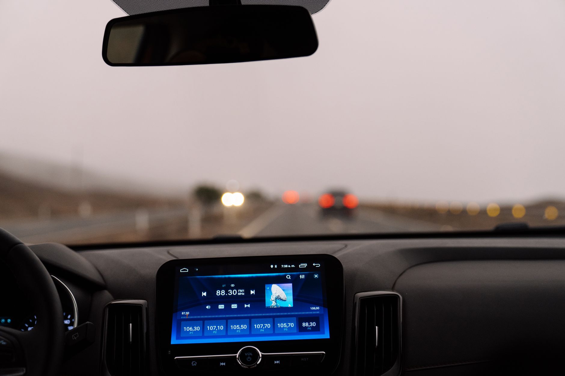 close-up of a vehicle dashboard-mounted toll transponder device affixed to a windshield, with a highway lane visible through the glass ahead