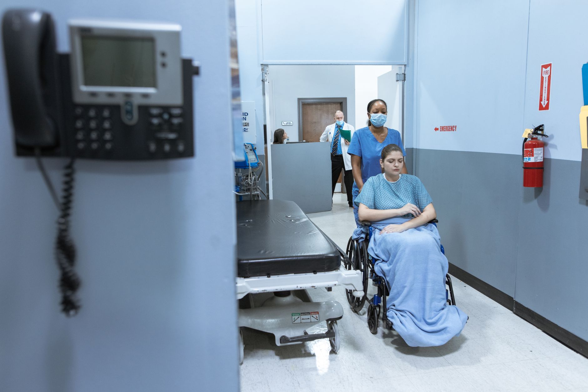 a hospital corridor at night with an unmanned nursing station and a tablet mounted on the wall displaying patient monitoring data
