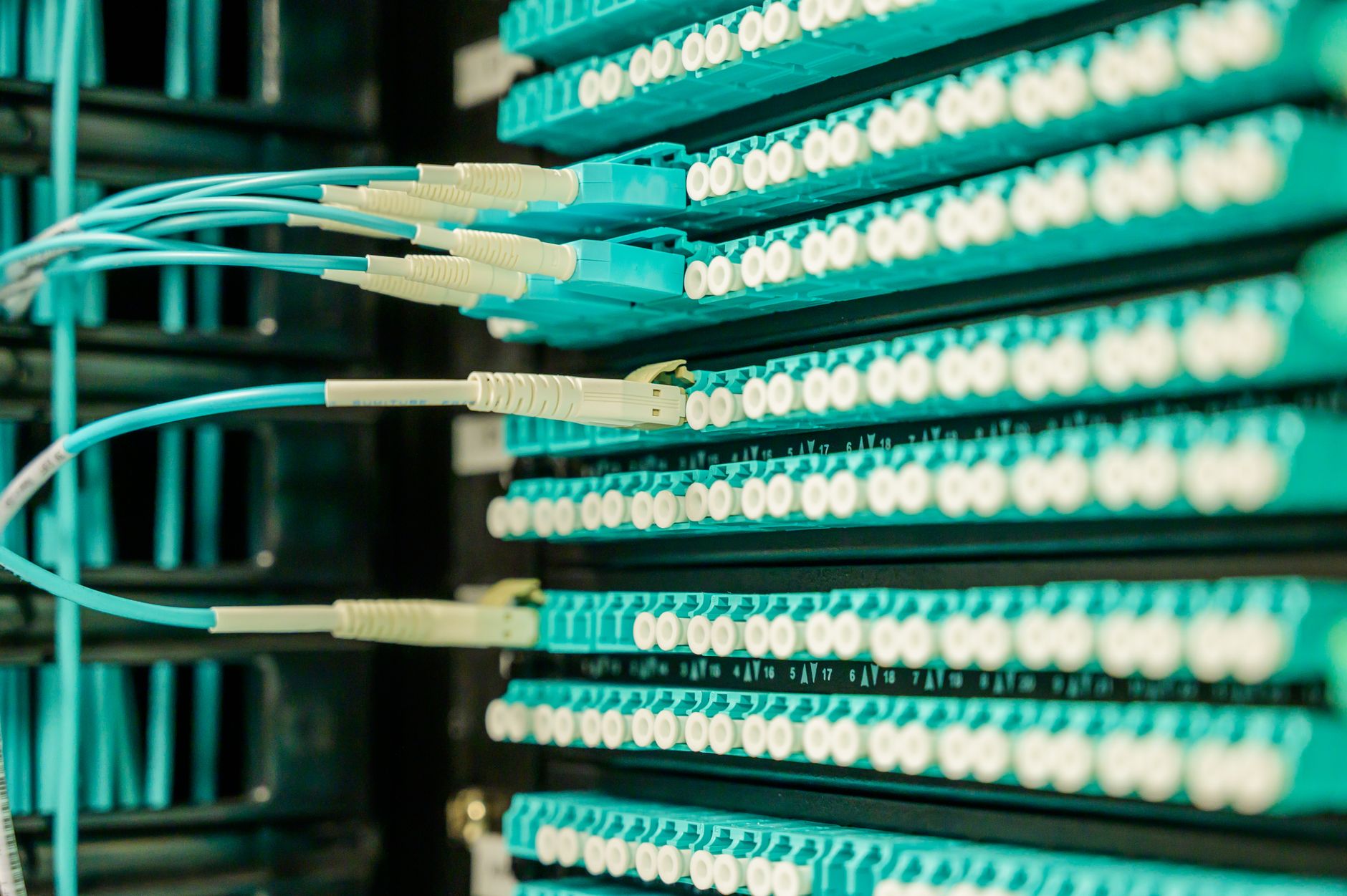 a telecommunications data center corridor with rows of rack-mounted networking hardware and fiber optic cable bundles running along the ceiling