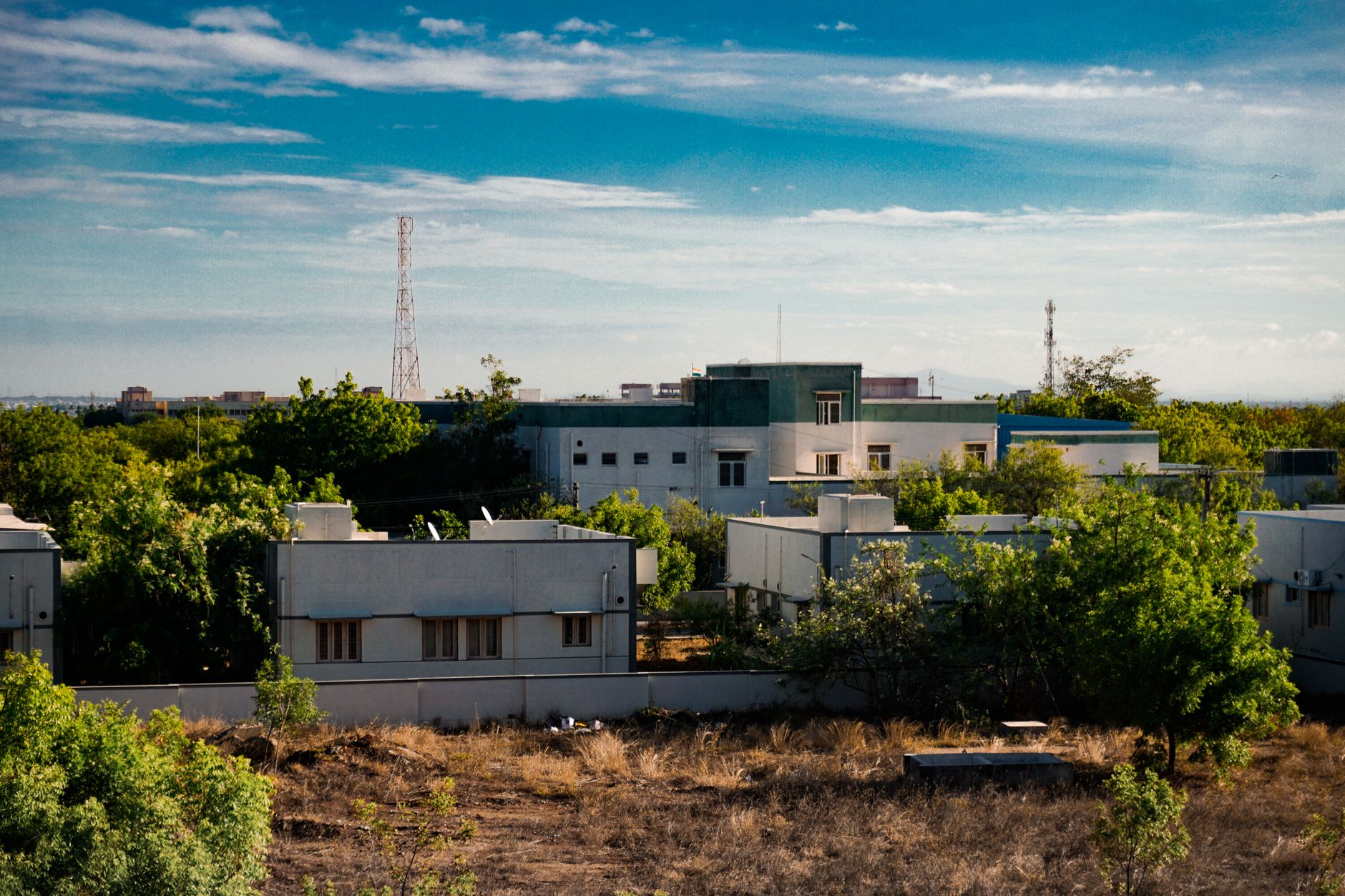 aerial view of a modern low-rise tech campus surrounded by landscaped grounds in an urban Israeli setting, late afternoon light casting long shadows across the buildings
