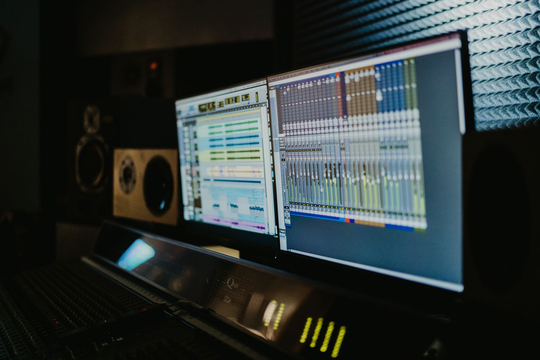 a wide-angle view of a creative studio workspace with digital drawing tablets, audio production equipment, and multiple monitors displaying waveforms and vector art software