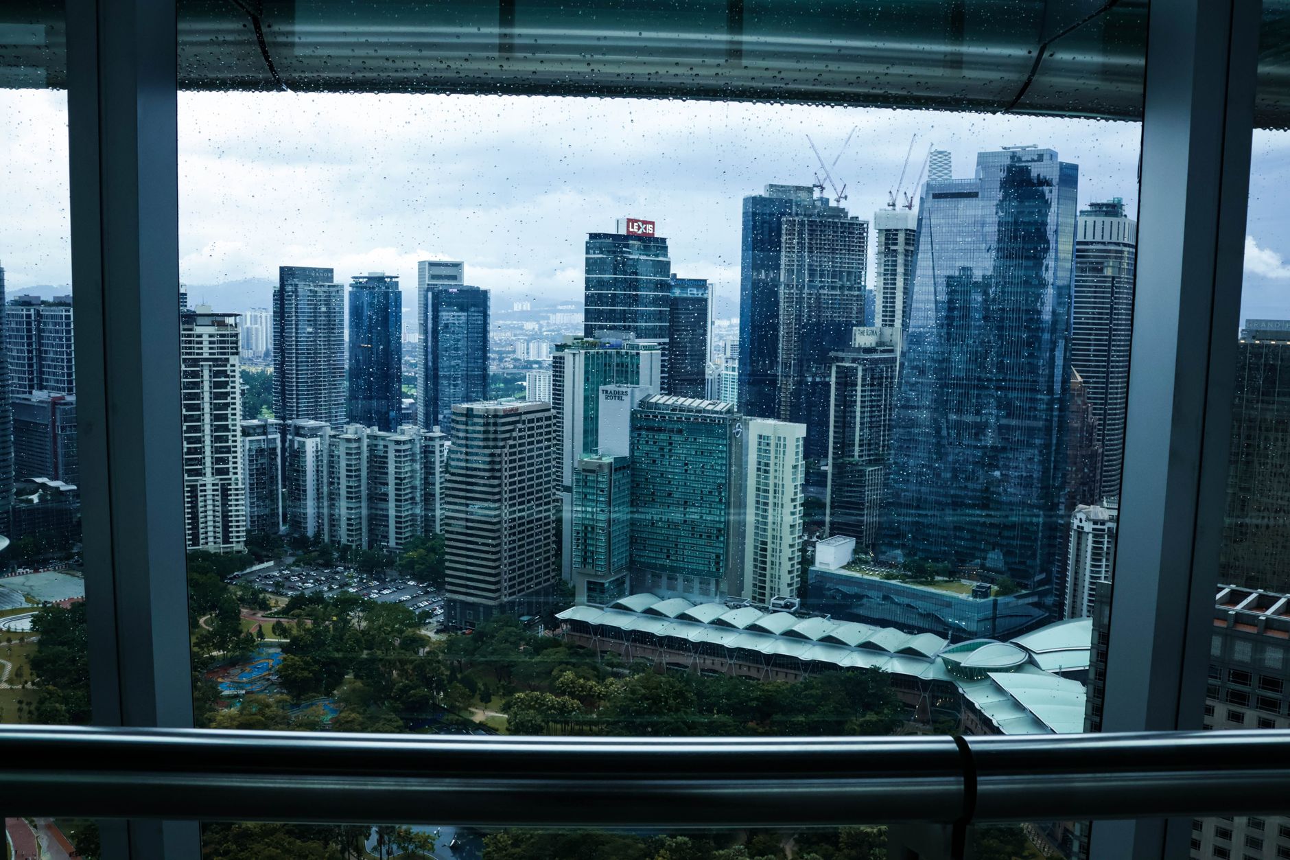 wide-angle shot of a modern convention center exterior in Kuala Lumpur with glass facades reflecting afternoon light, surrounded by urban skyline