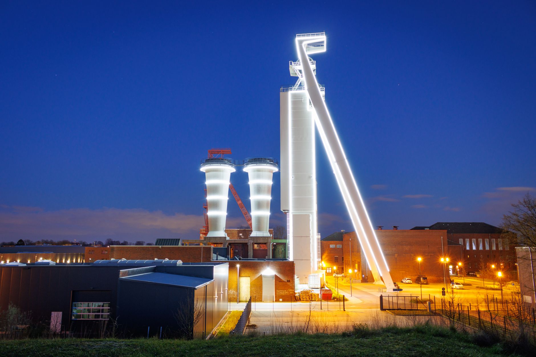 aerial view of a large semiconductor fabrication plant complex at dusk, with lit cleanroom windows and industrial infrastructure visible