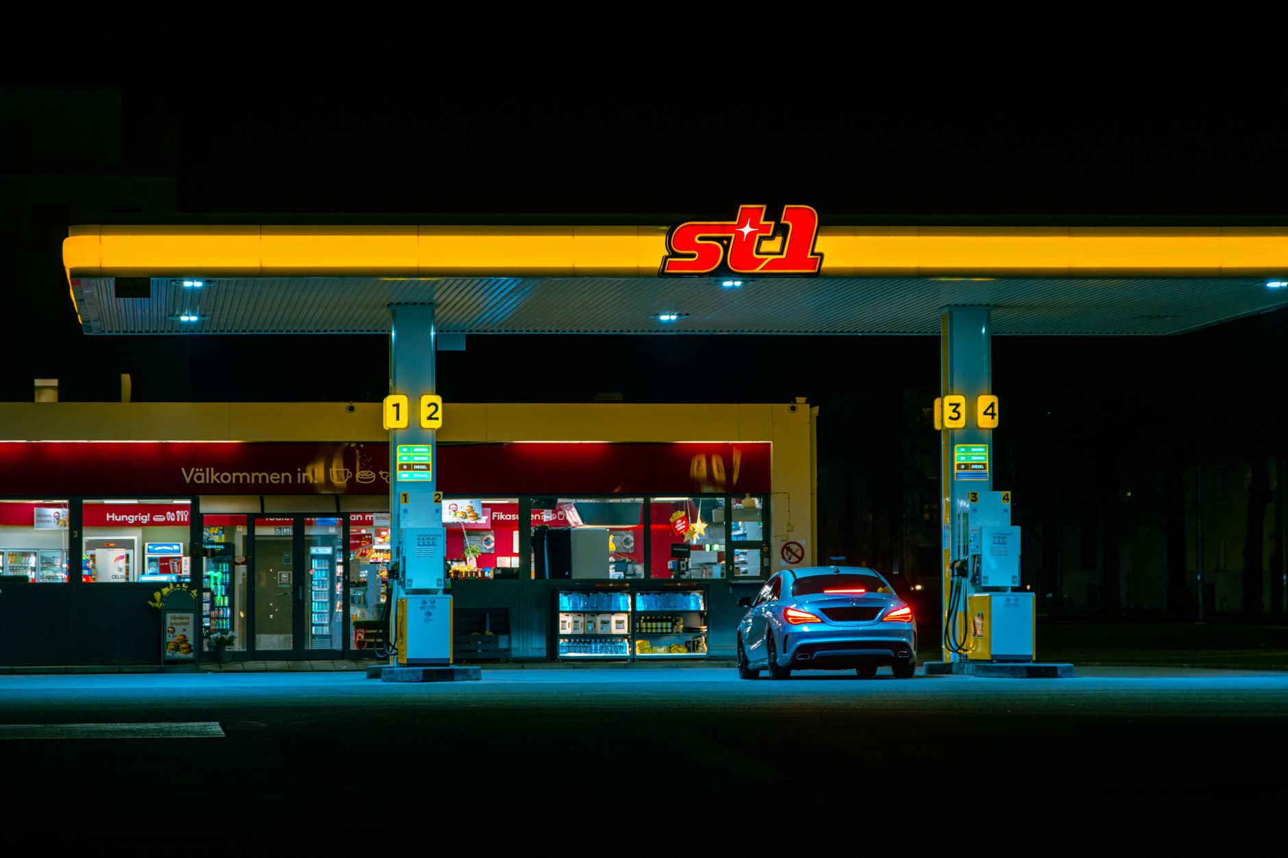 exterior of a small rural convenience store with a hand-painted sign, gas pumps visible in the foreground on a quiet two-lane road