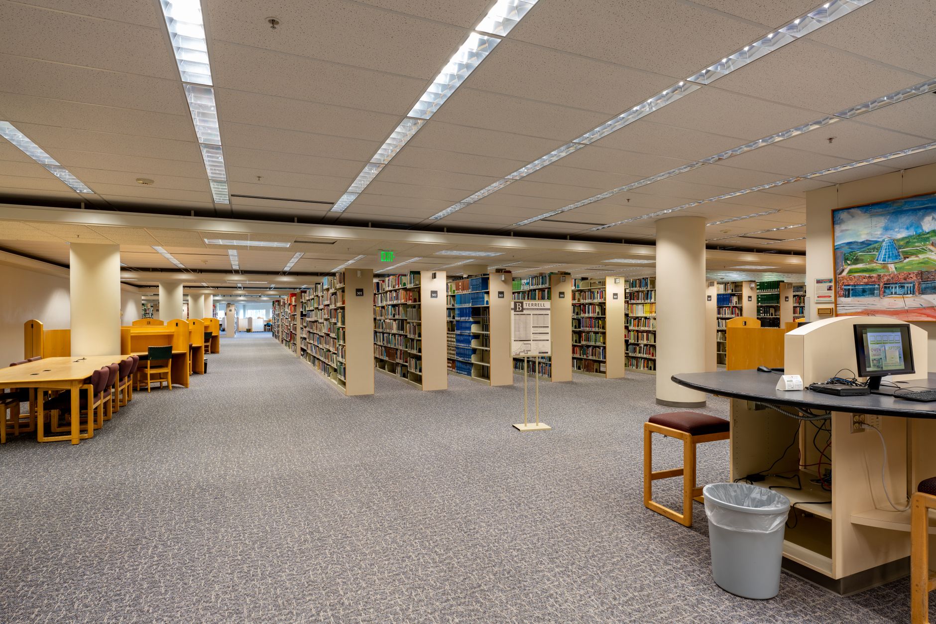 rows of desktop computers in a modern university computer lab with large windows overlooking a campus courtyard