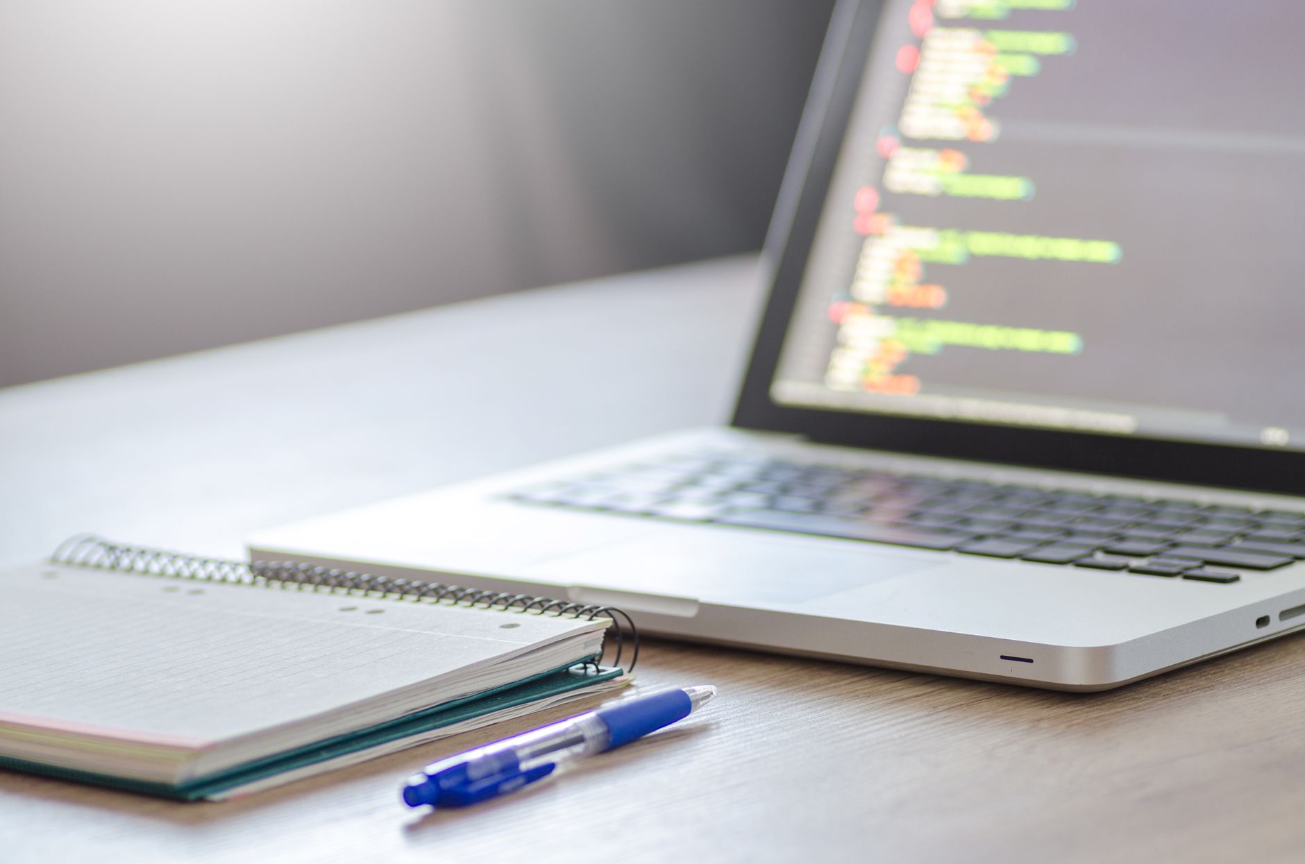 a clean desk setup with a laptop open to a terminal window showing lines of autonomously generated and executed code scrolling in real time, beside a coffee cup and notebook