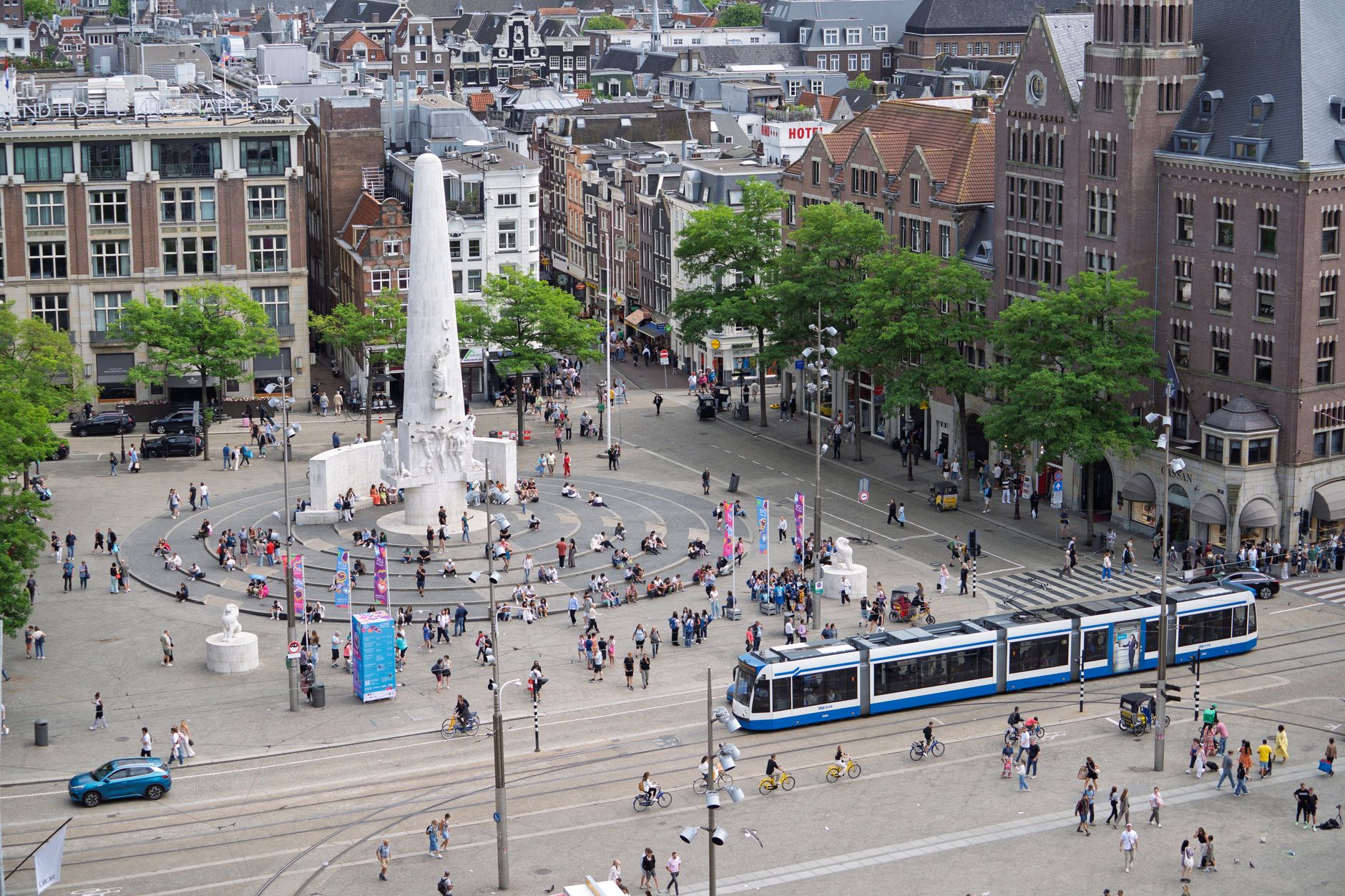 a wide-angle view of a European city square with large-format outdoor advertising displays mounted on building facades, pedestrians and trams passing below