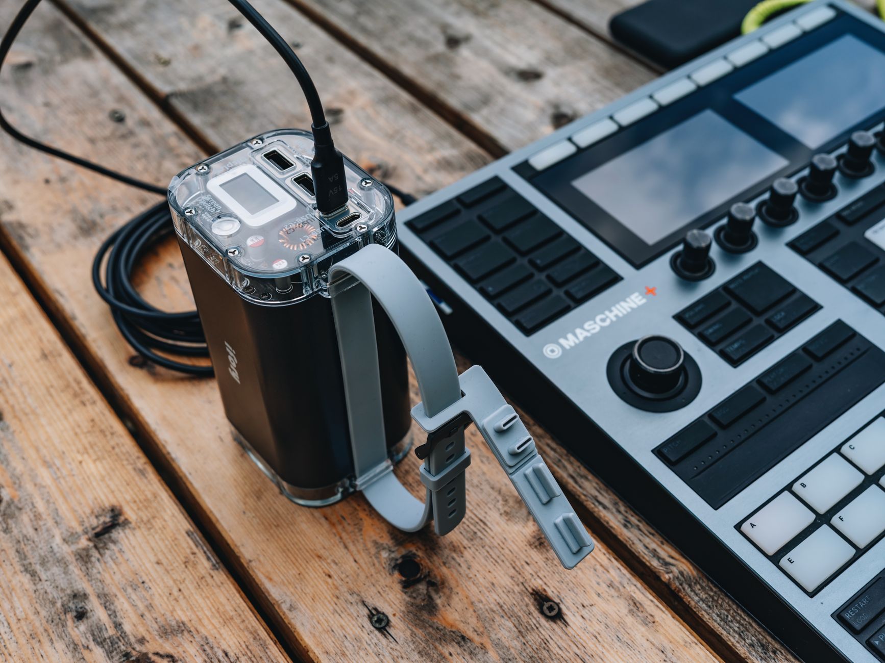 a compact military-grade battery pack sitting on a workbench in a research lab, with testing cables attached and diagnostic screens visible in the background