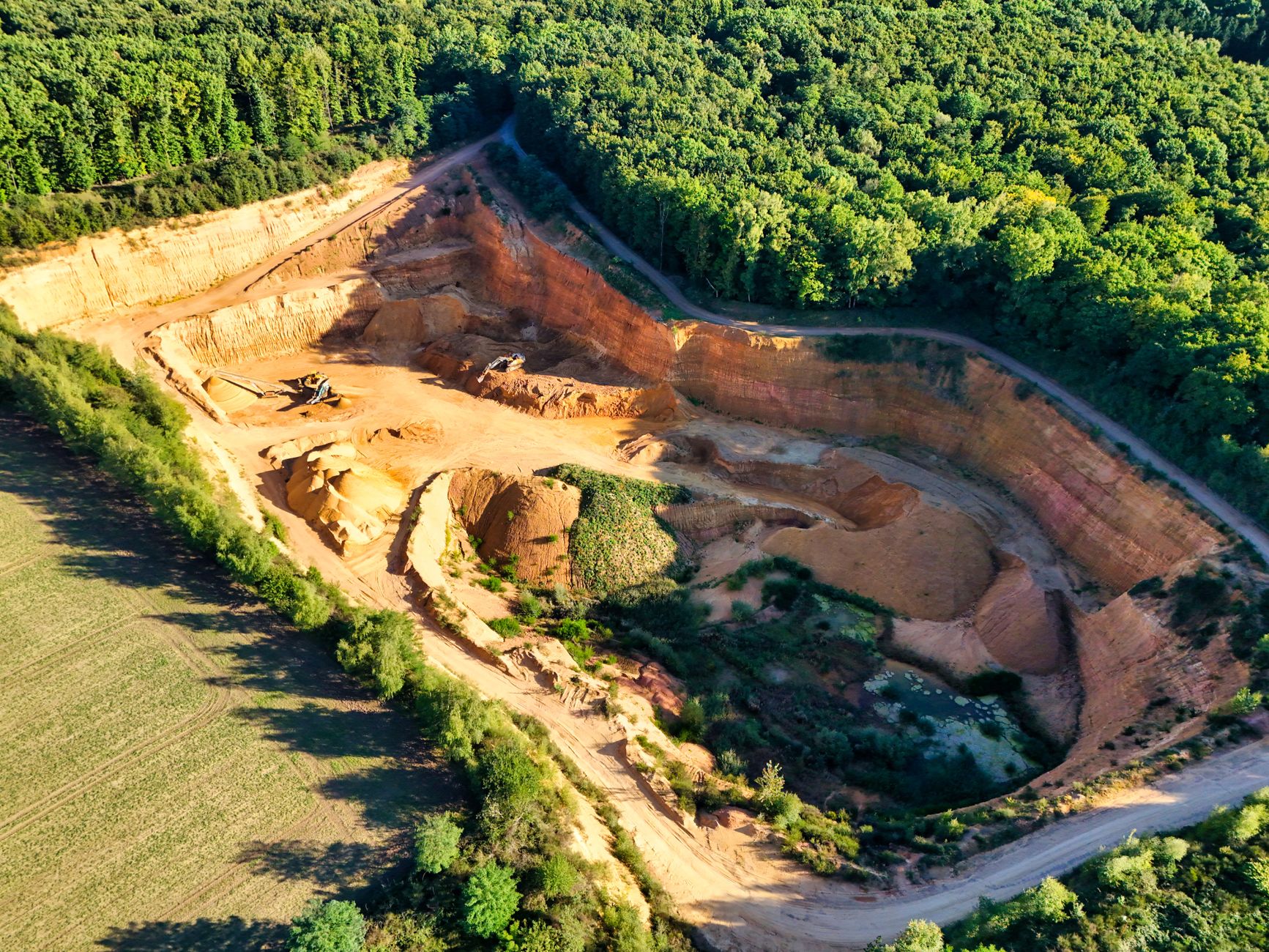aerial view of an open-pit copper-gold mine carved into forested hillside terrain in northern Greece, with processing facilities and haul roads visible below