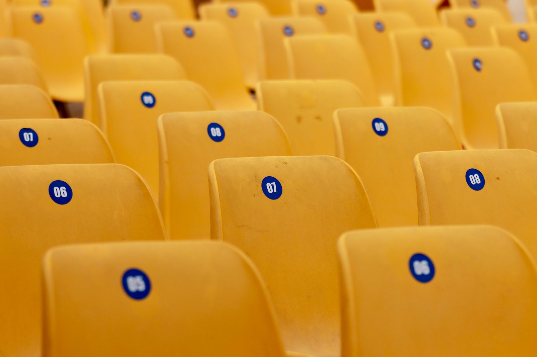 rows of vacant stadium seating in an indoor sports venue, overhead scoreboards dark, the playing surface below unoccupied and brightly lit