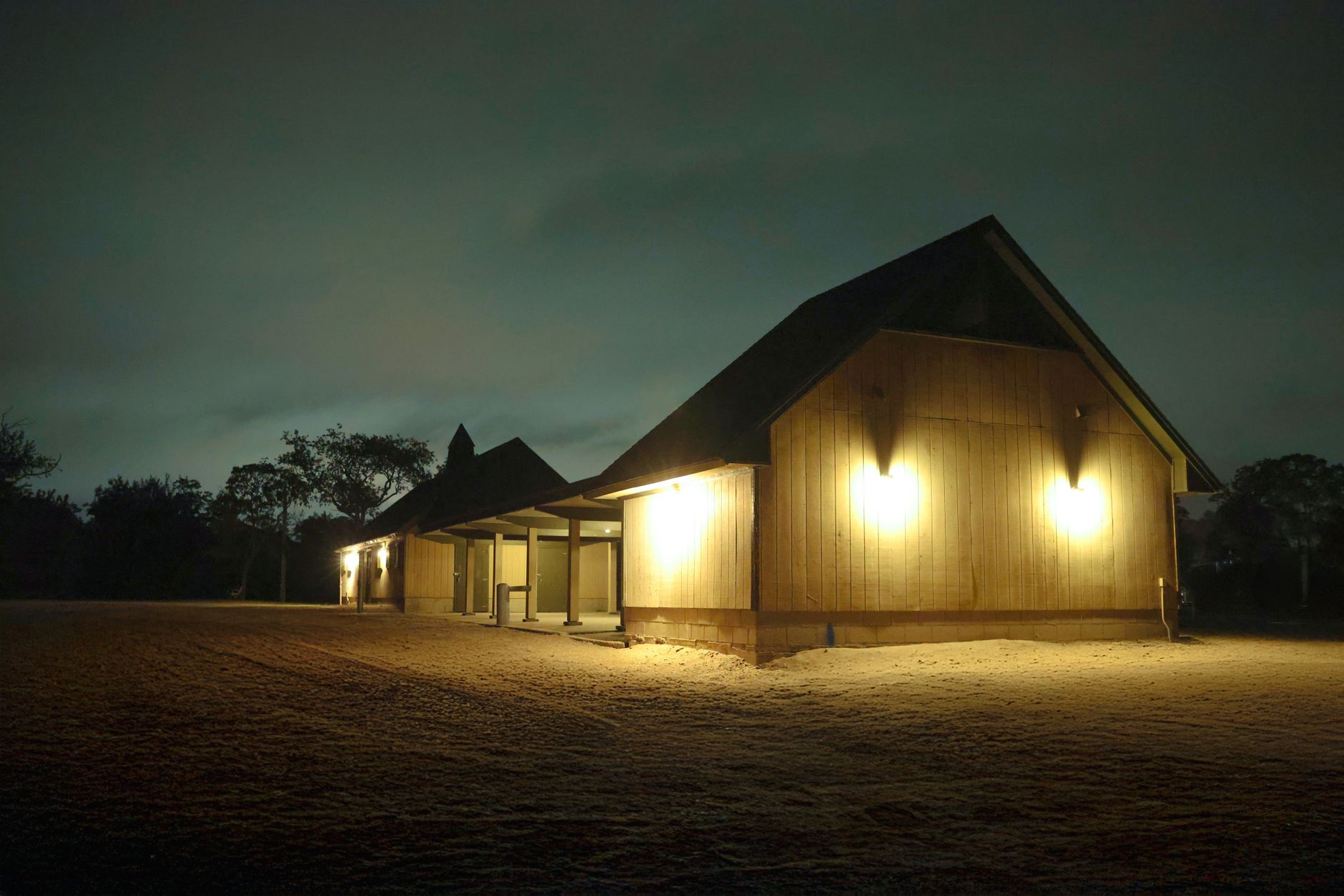 a small biotech company's research facility exterior at dusk, with laboratory windows lit from inside and a quiet parking area in the foreground