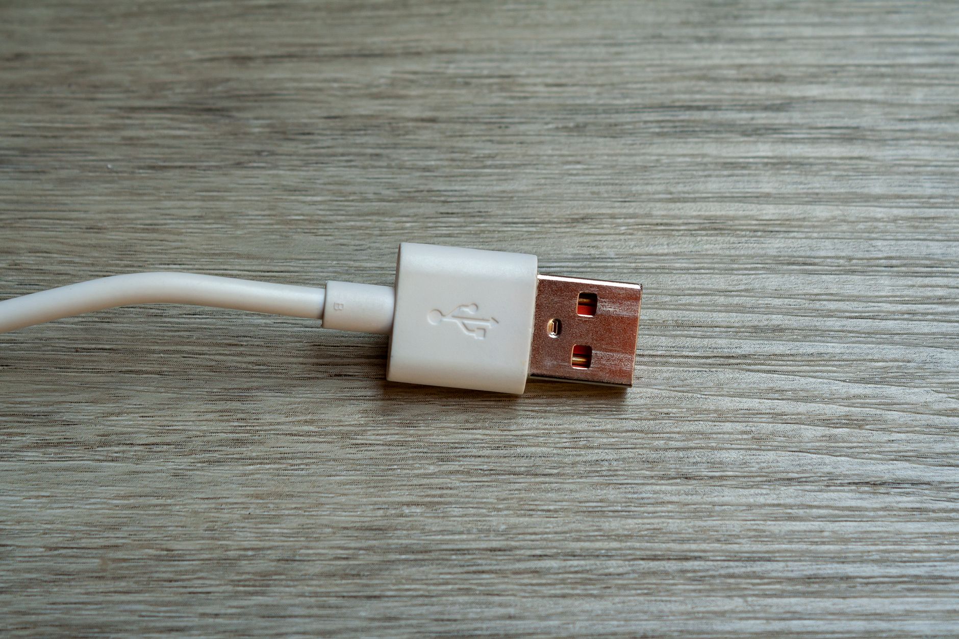 A Framework Laptop 13 closed on a minimalist desk surface, power LED unlit, with a charging cable connected