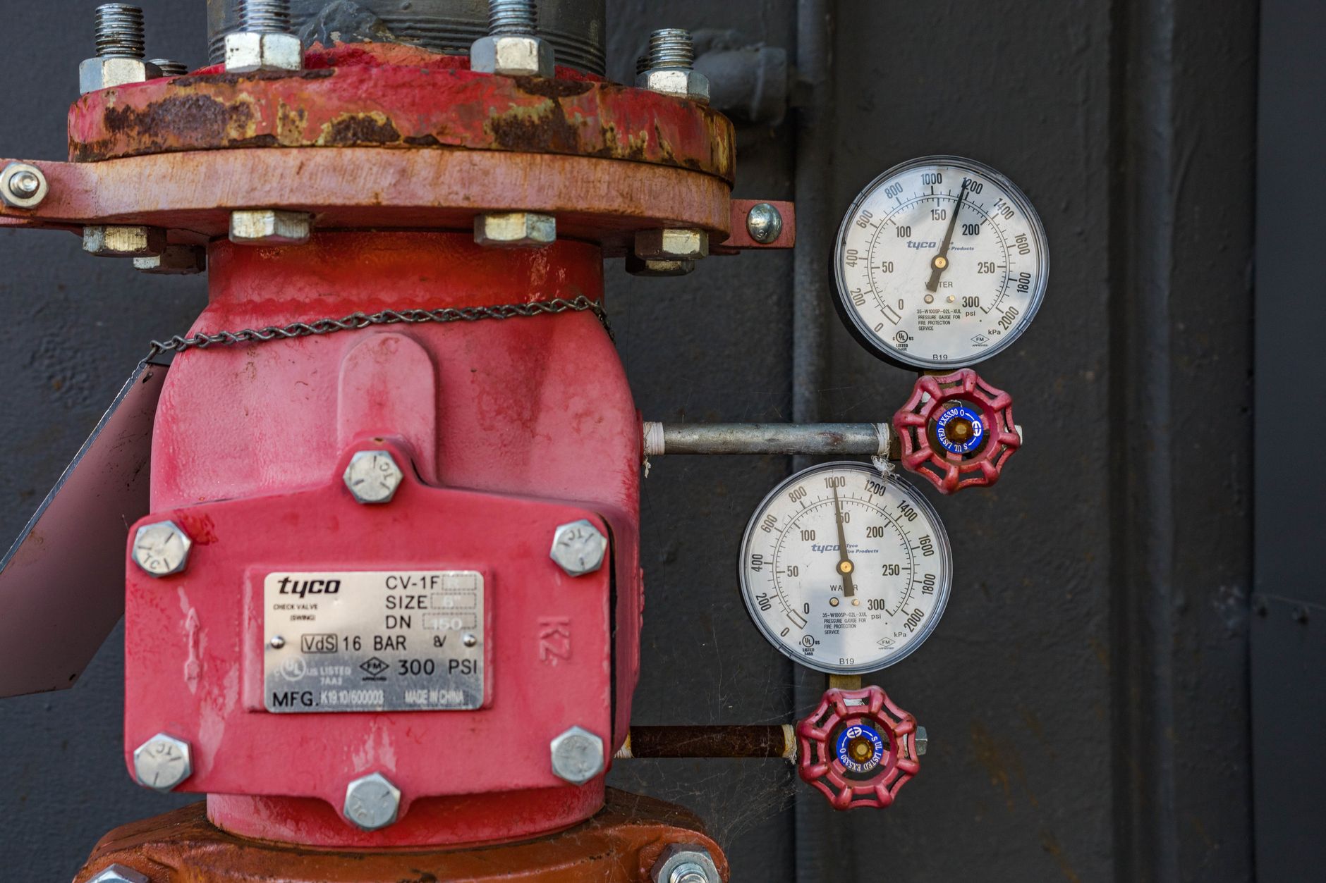 close-up of an industrial gas detection unit mounted on a metal pipeline inside a petrochemical processing facility, warning indicator lights visible on the panel