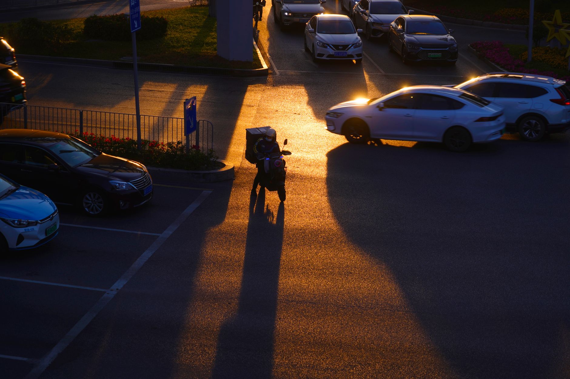 a delivery scooter parked outside a busy urban warehouse loading dock, late afternoon light casting long shadows across the pavement