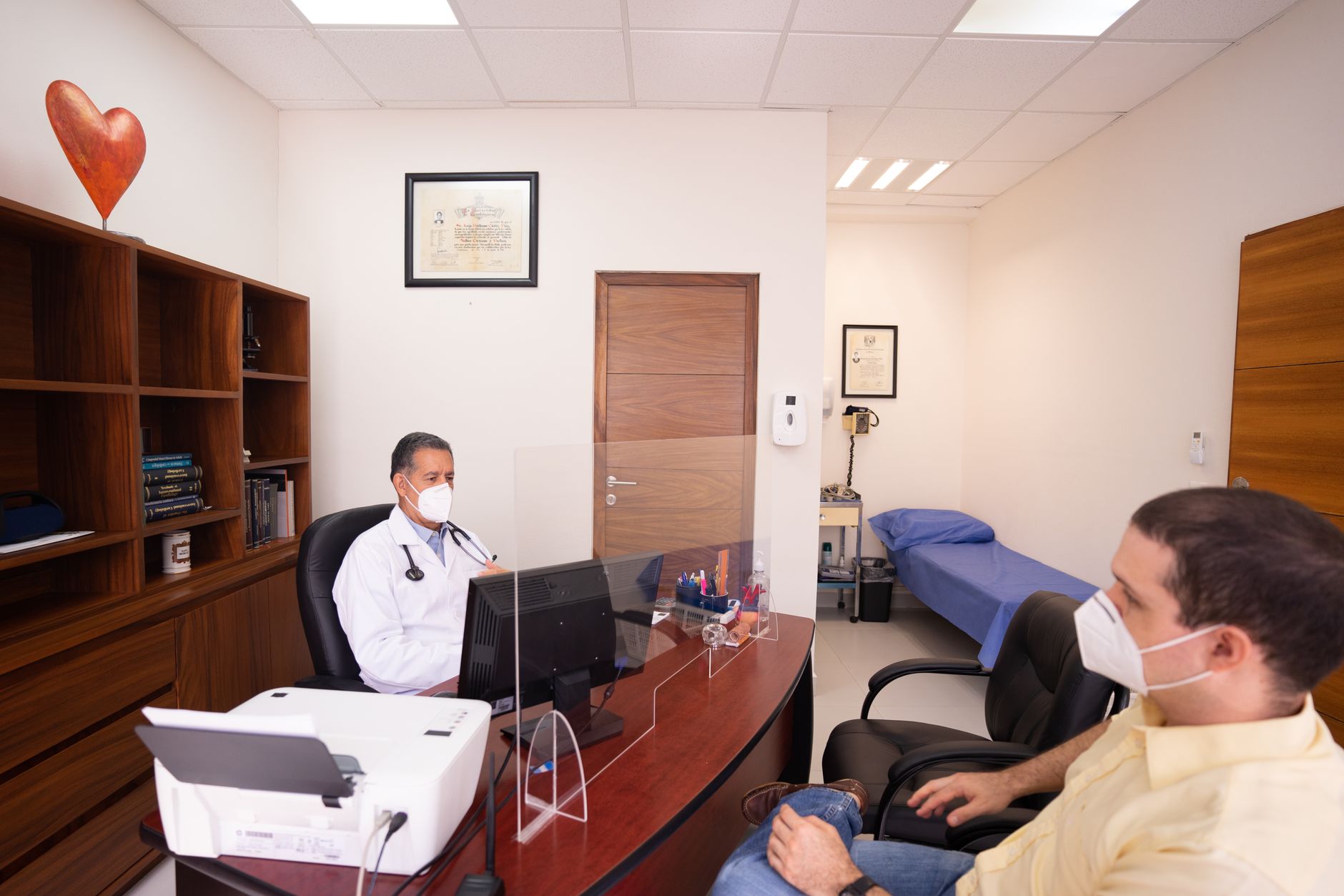 a modern physician office exam room with a large wall-mounted digital display showing health information content, medical equipment visible in the background