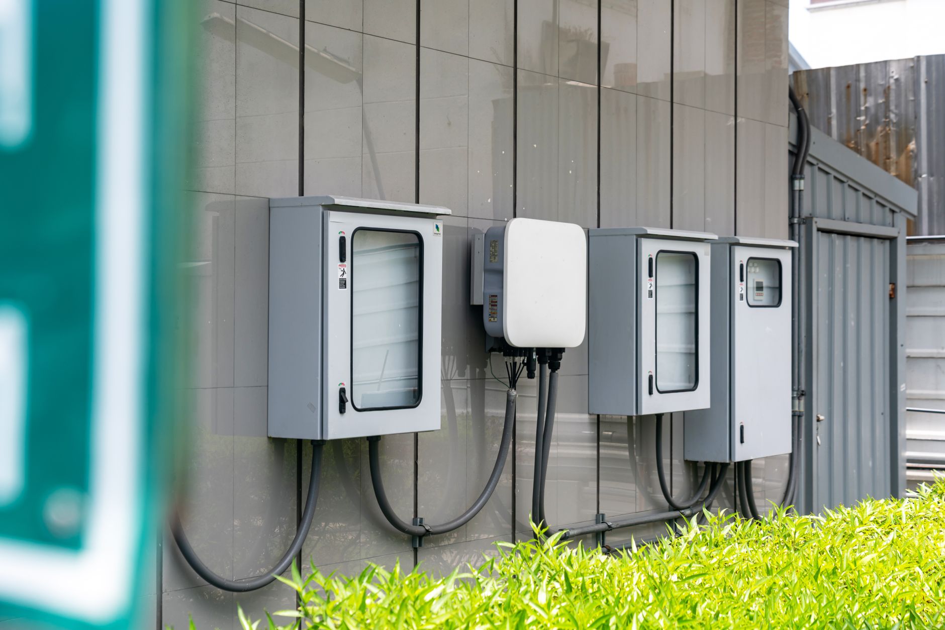 rows of industrial cooling units along the exterior wall of a data center building on a gray overcast day, with utility infrastructure visible in the background