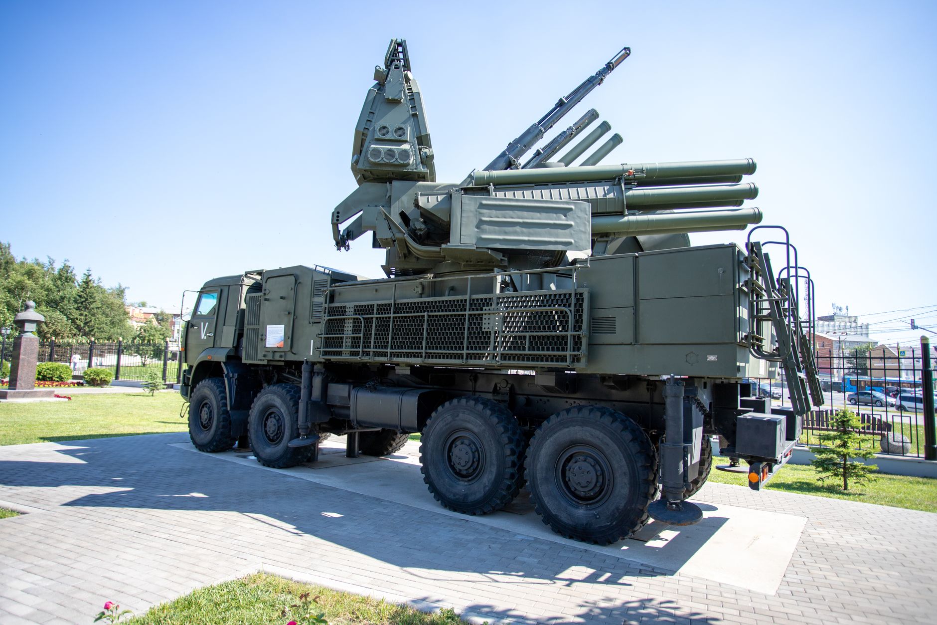 an outdoor launch facility with a large surface-to-air missile system on its elevated rail platform against a clear sky, launch support infrastructure visible in the background