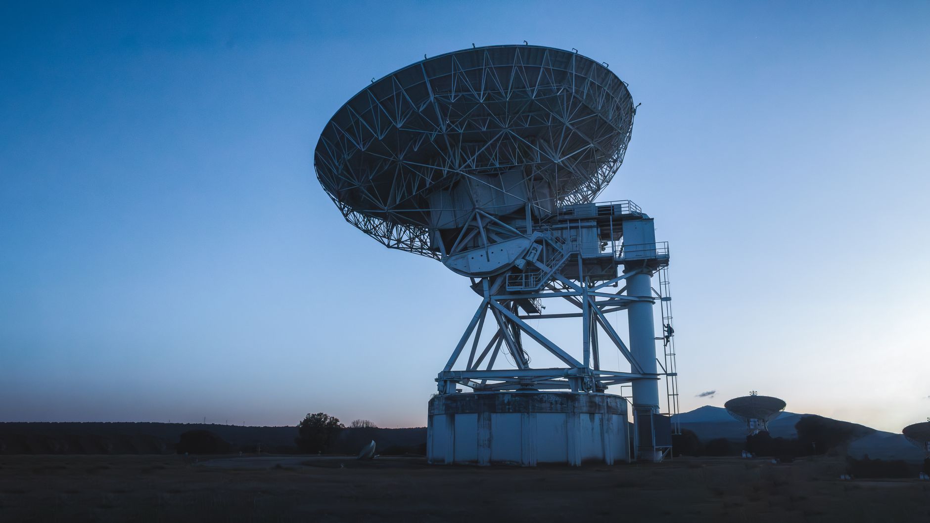 rows of radar antenna arrays and ground-based sensor equipment at a military air defense installation, set against a flat desert landscape at dusk