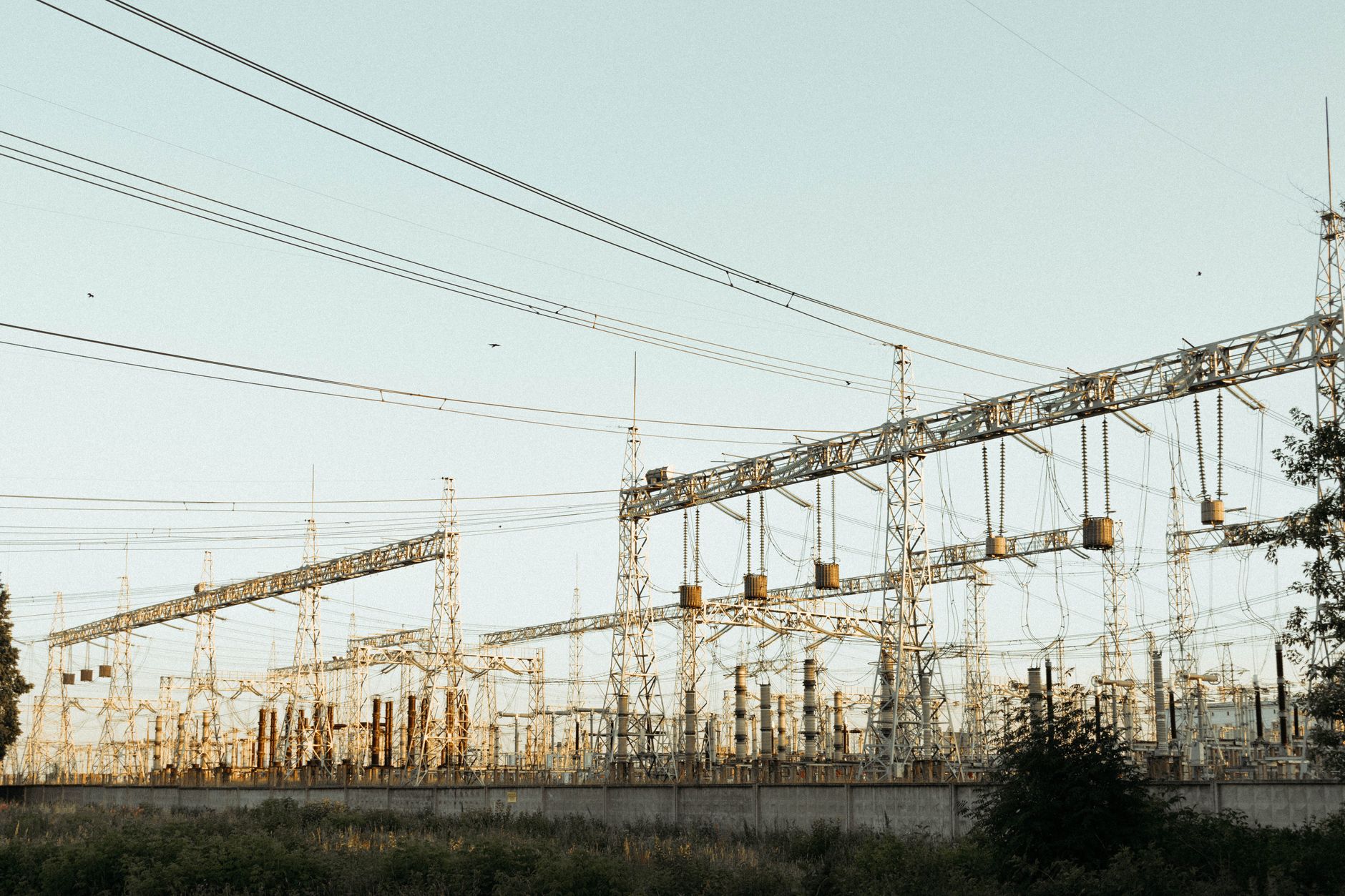 overhead view of a large electrical substation with transformer banks and high-voltage transmission lines stretching toward the horizon at dusk