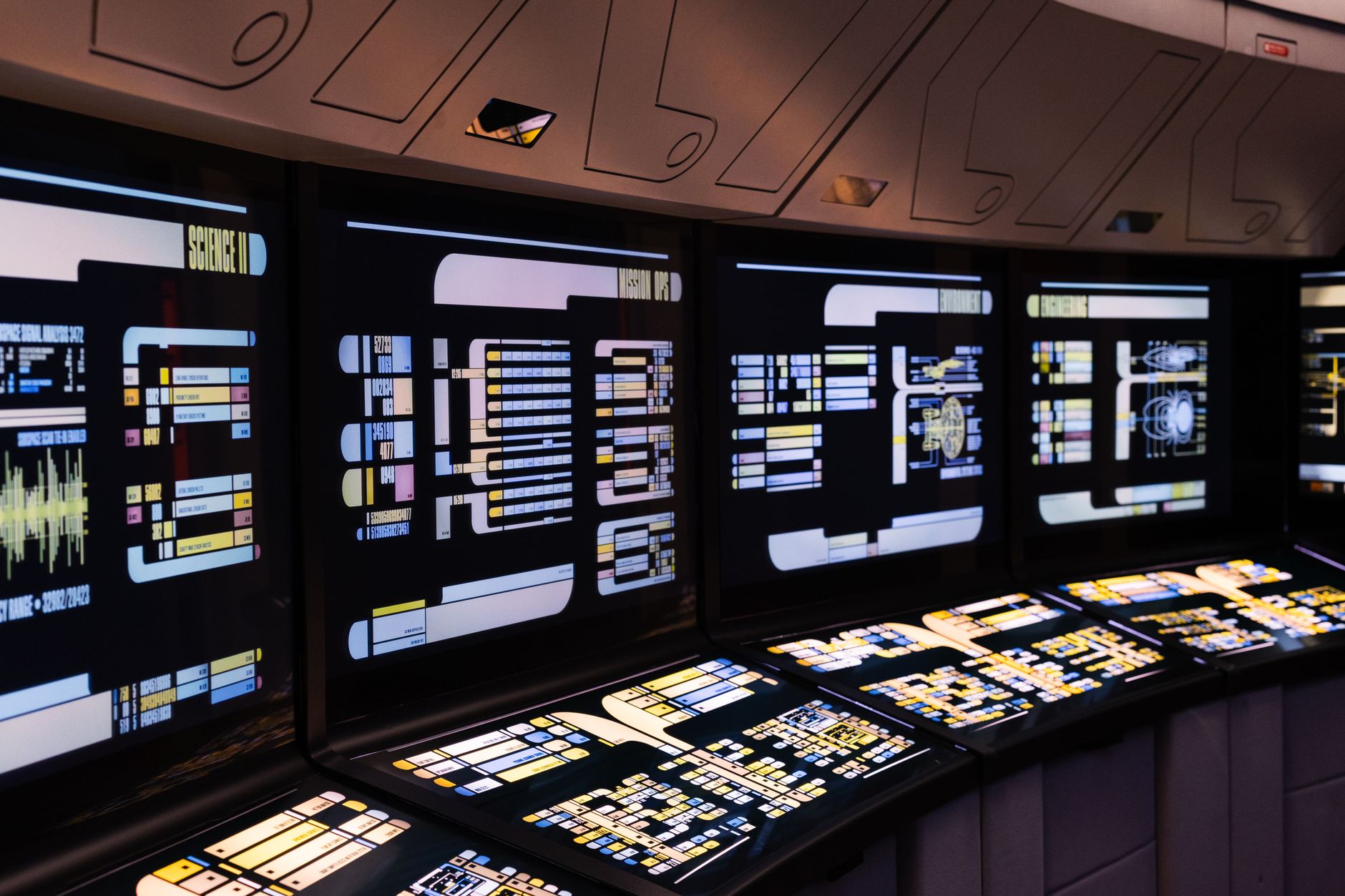 rows of workstations in a technology studio space with large screens displaying product roadmaps and analytics interfaces, natural light coming through windows