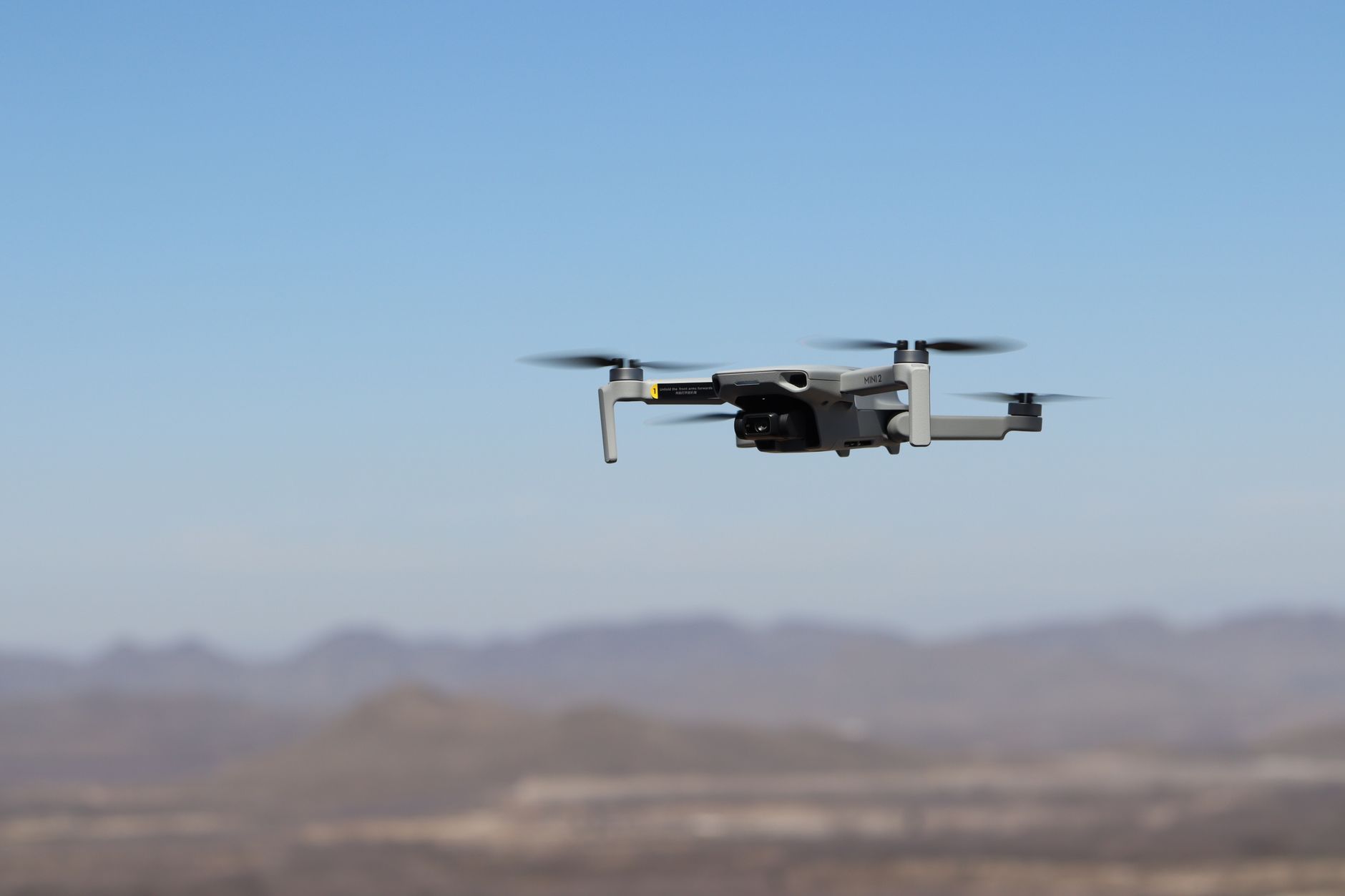 a thermal imaging camera mounted on a military surveillance drone hovering above an arid desert landscape at dusk
