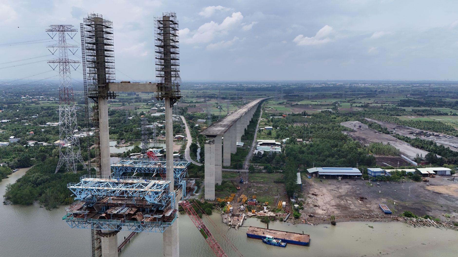 aerial view of a large-scale data center campus under construction, surrounded by open land with power transmission lines visible in the distance