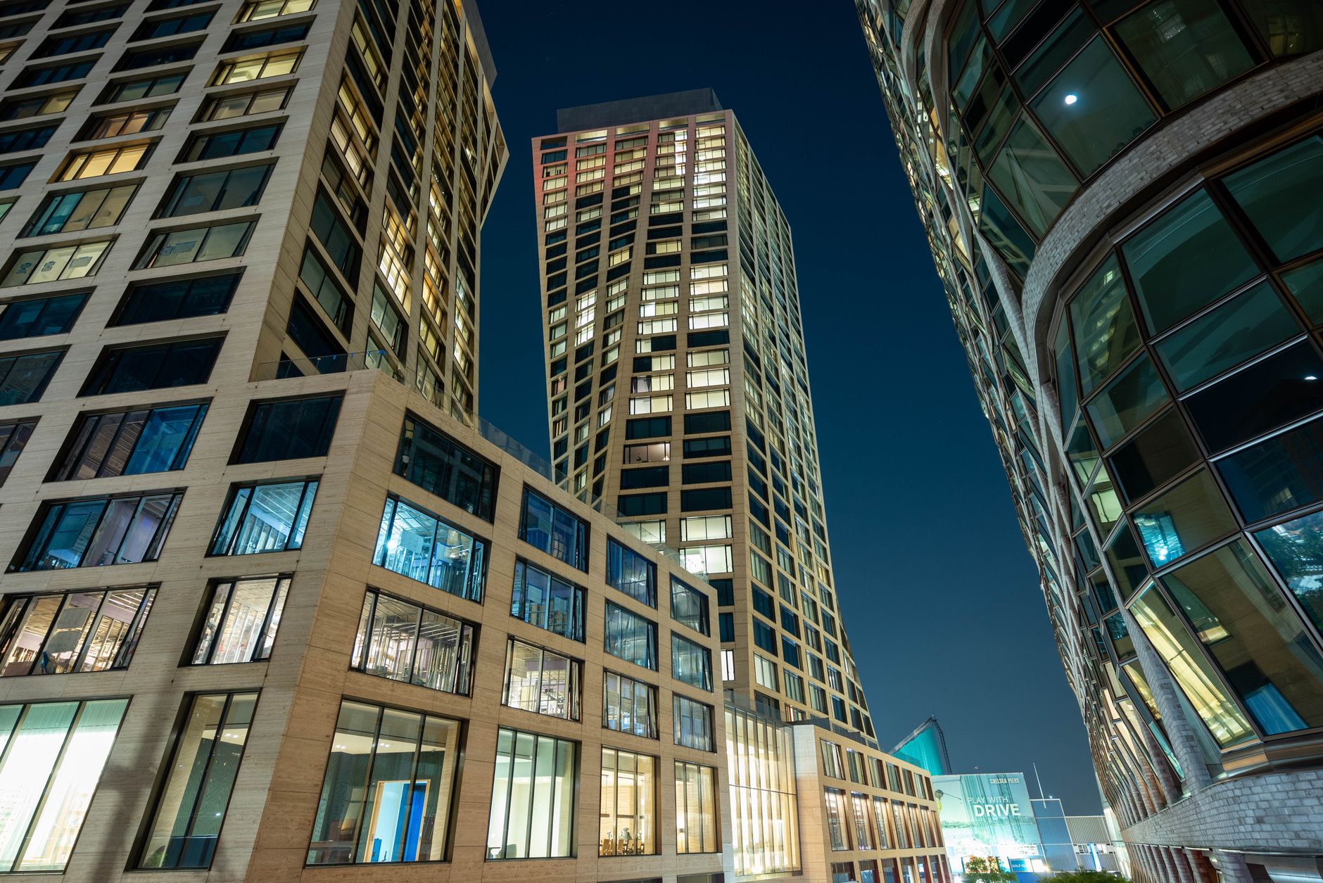 an aerial view of a high-tech office district at dusk, with illuminated glass buildings and urban streets below visible through floor-to-ceiling windows