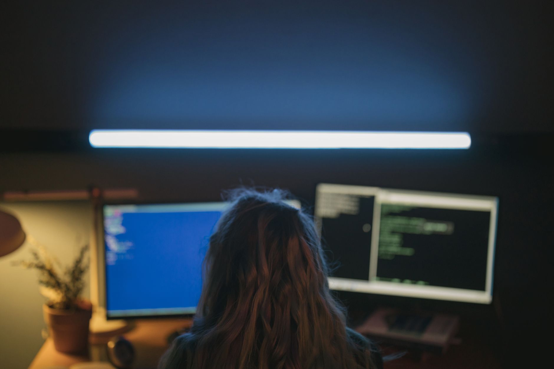 rows of standing desks with dual-monitor coding setups in a modern startup workspace, exposed concrete walls and overhead LED lighting