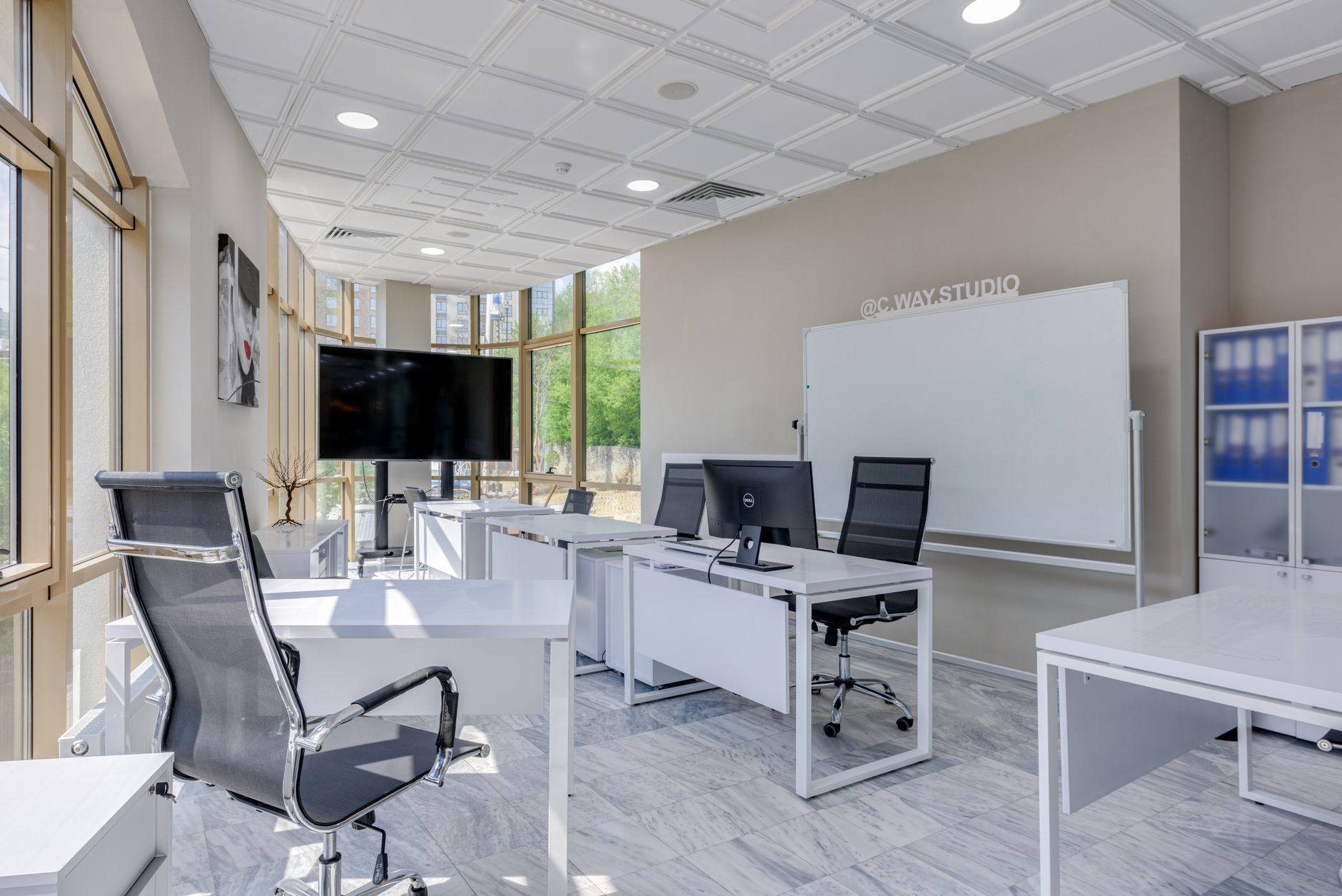 a wide-angle shot of a modern co-working office space with multiple monitors displaying financial spreadsheets and startup pitch slide decks, empty chairs and natural light coming through floor-to-ceiling windows