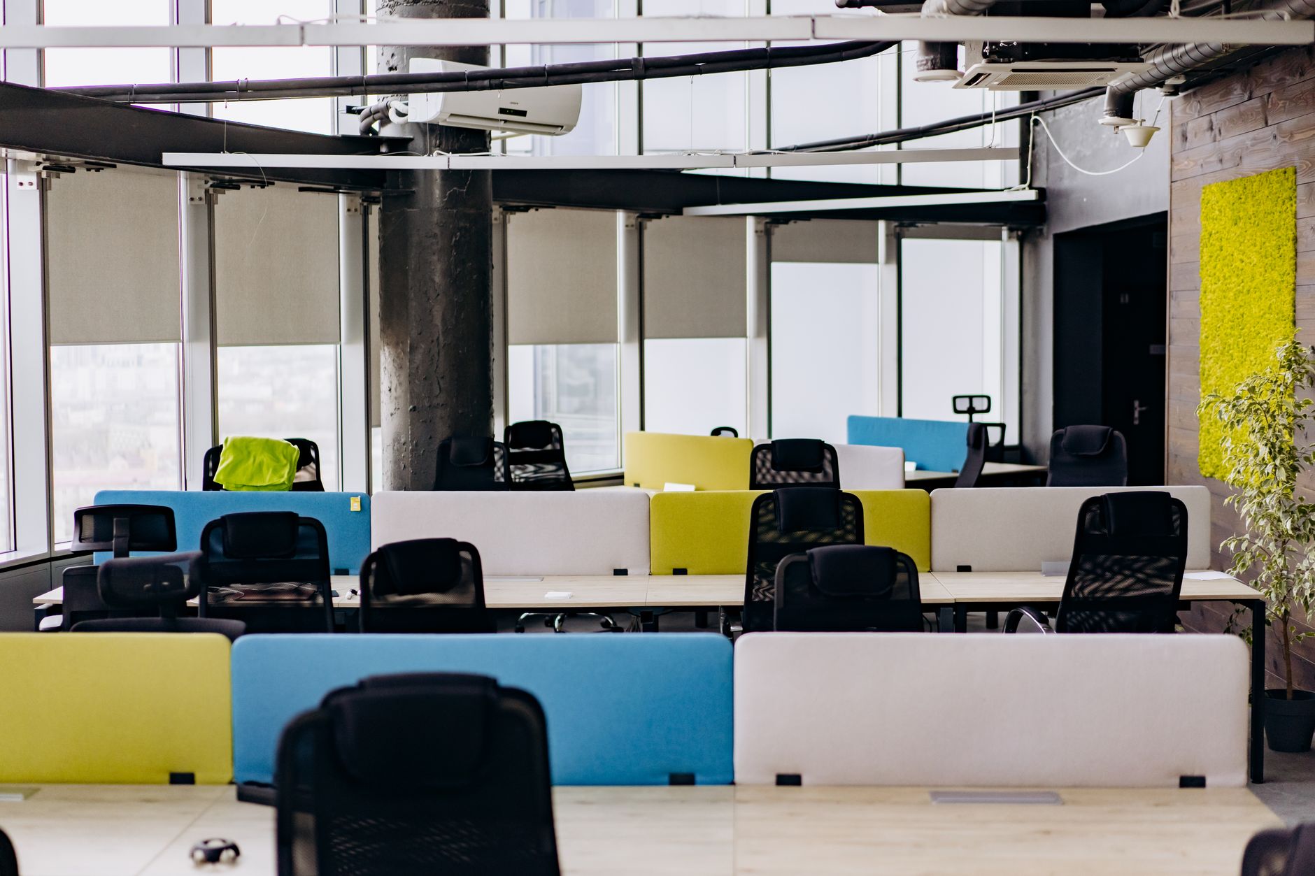 a modern co-working office with floor-to-ceiling windows overlooking a city skyline, rows of standing desks with monitors displaying code and dashboards, natural light filling the space
