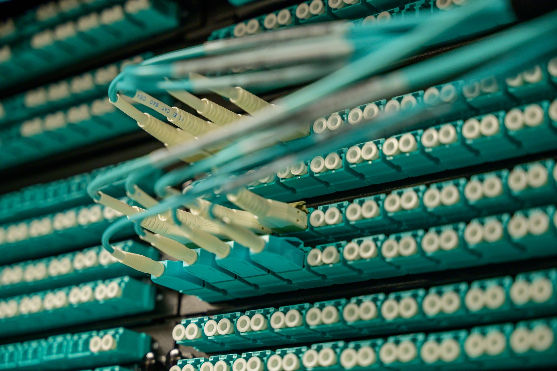 rows of enterprise-grade server racks inside a large, brightly lit data center corridor, cable bundles running along the ceiling
