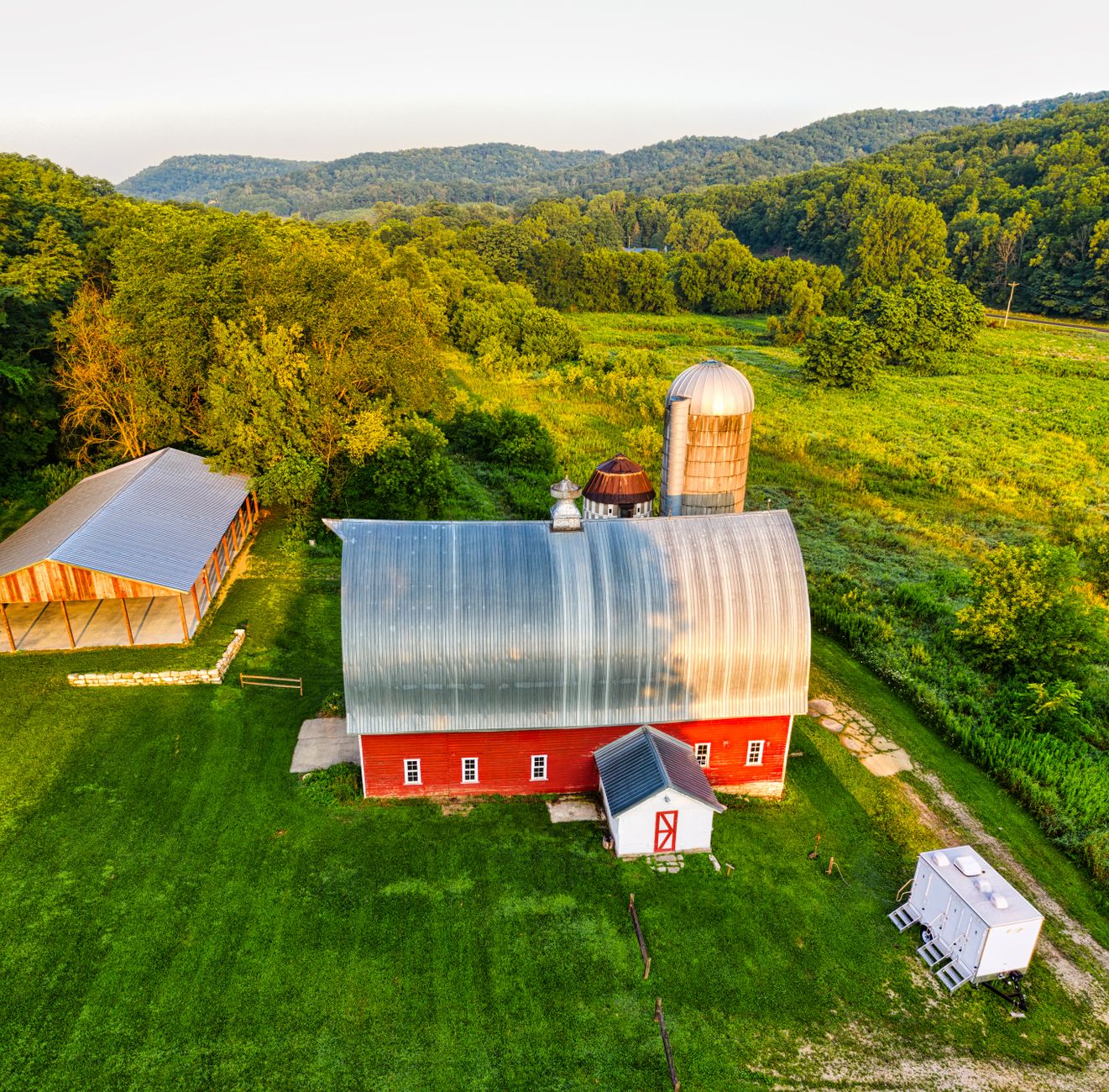 wide aerial view of a traditional Kentucky farm with rolling fields, a weathered barn, and fenced pastures in late afternoon light, no people visible