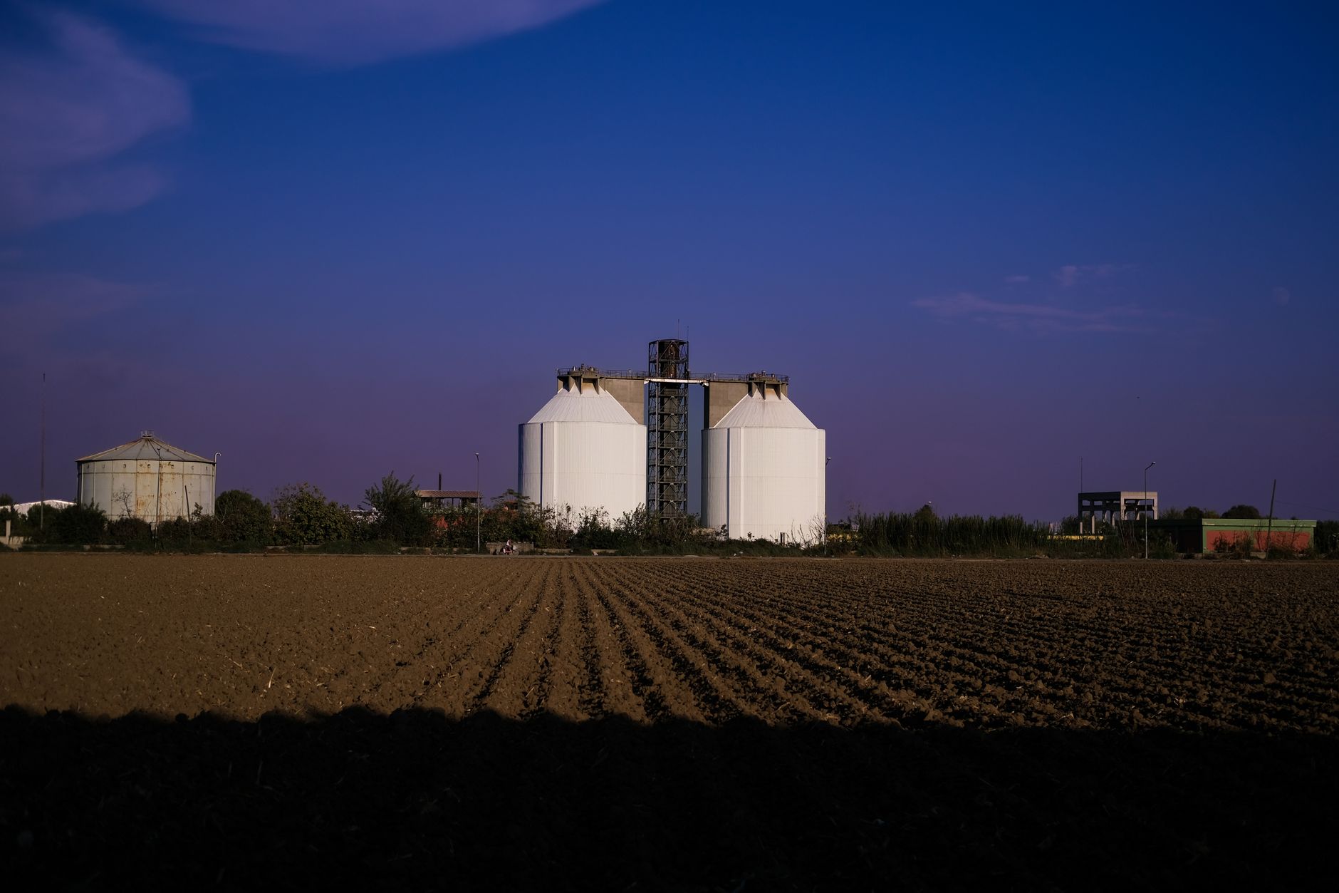 rows of gray modular data center containers lined up outside a facility near a rural landscape, late evening sky visible above