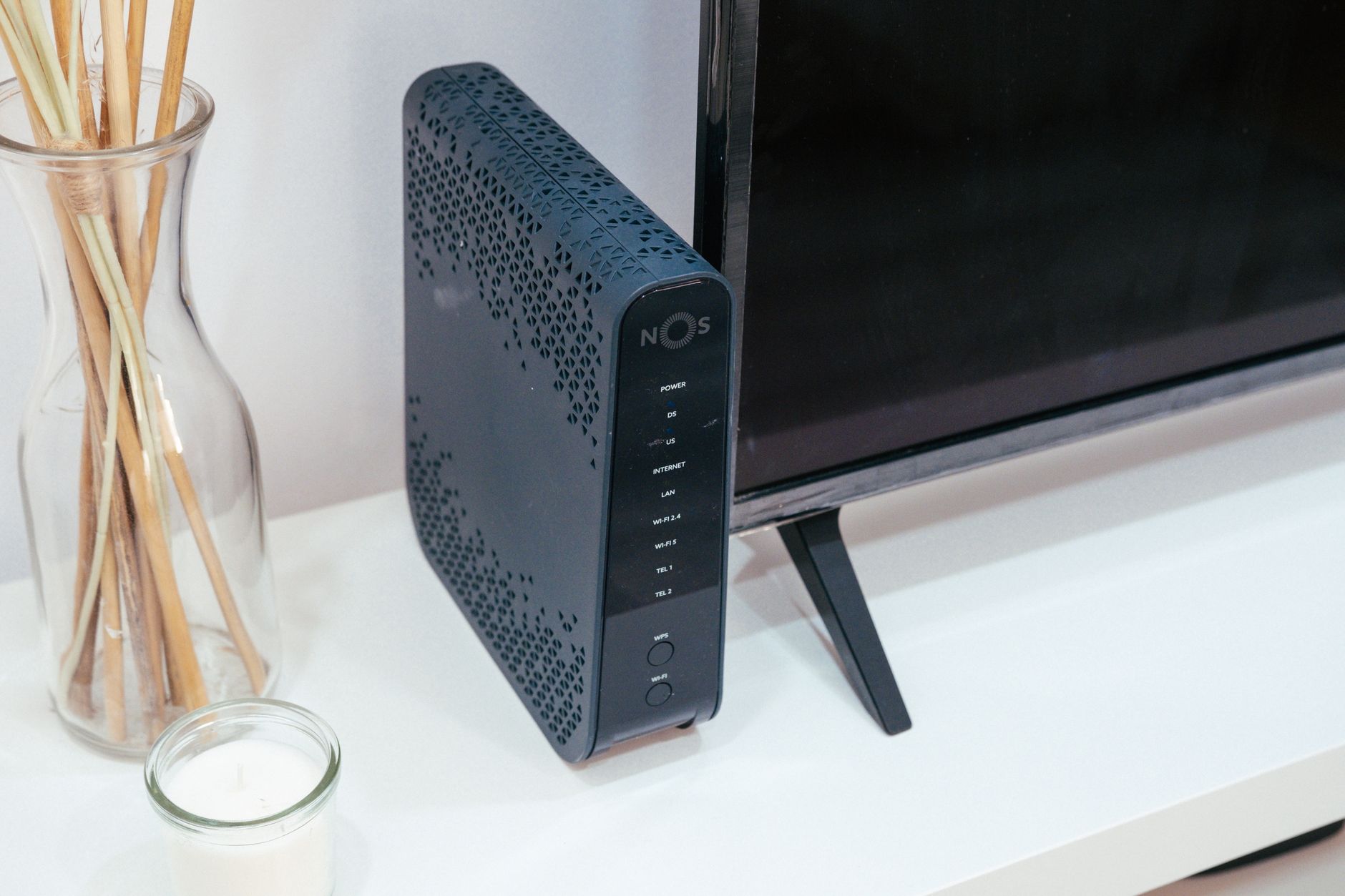 a modern flat-screen smart TV mounted on a living room wall displaying a generic streaming home screen, with a router visible on a shelf below it