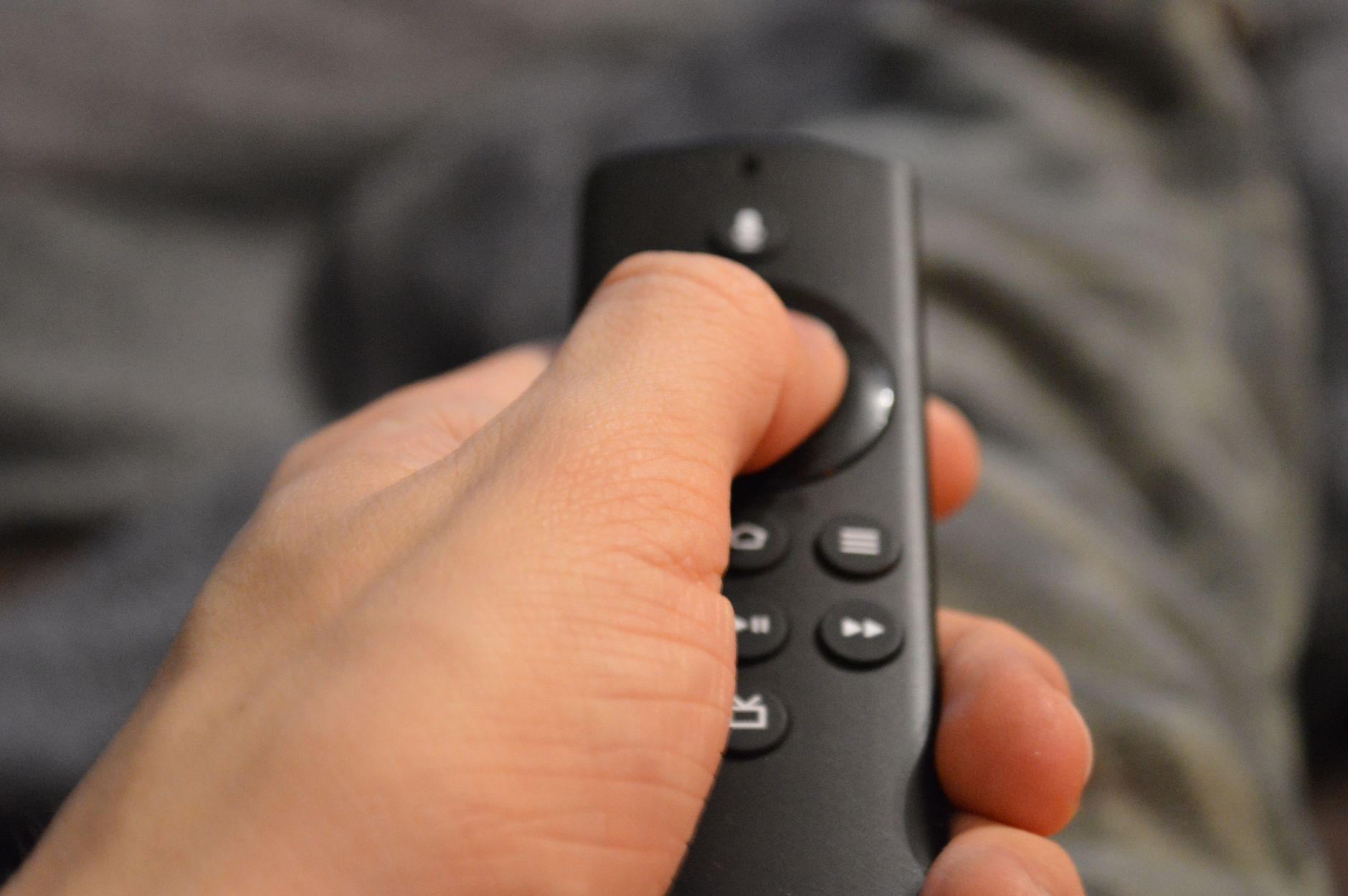 close-up of a smart TV remote resting on a couch armrest with the television's ambient backlight faintly visible in the background