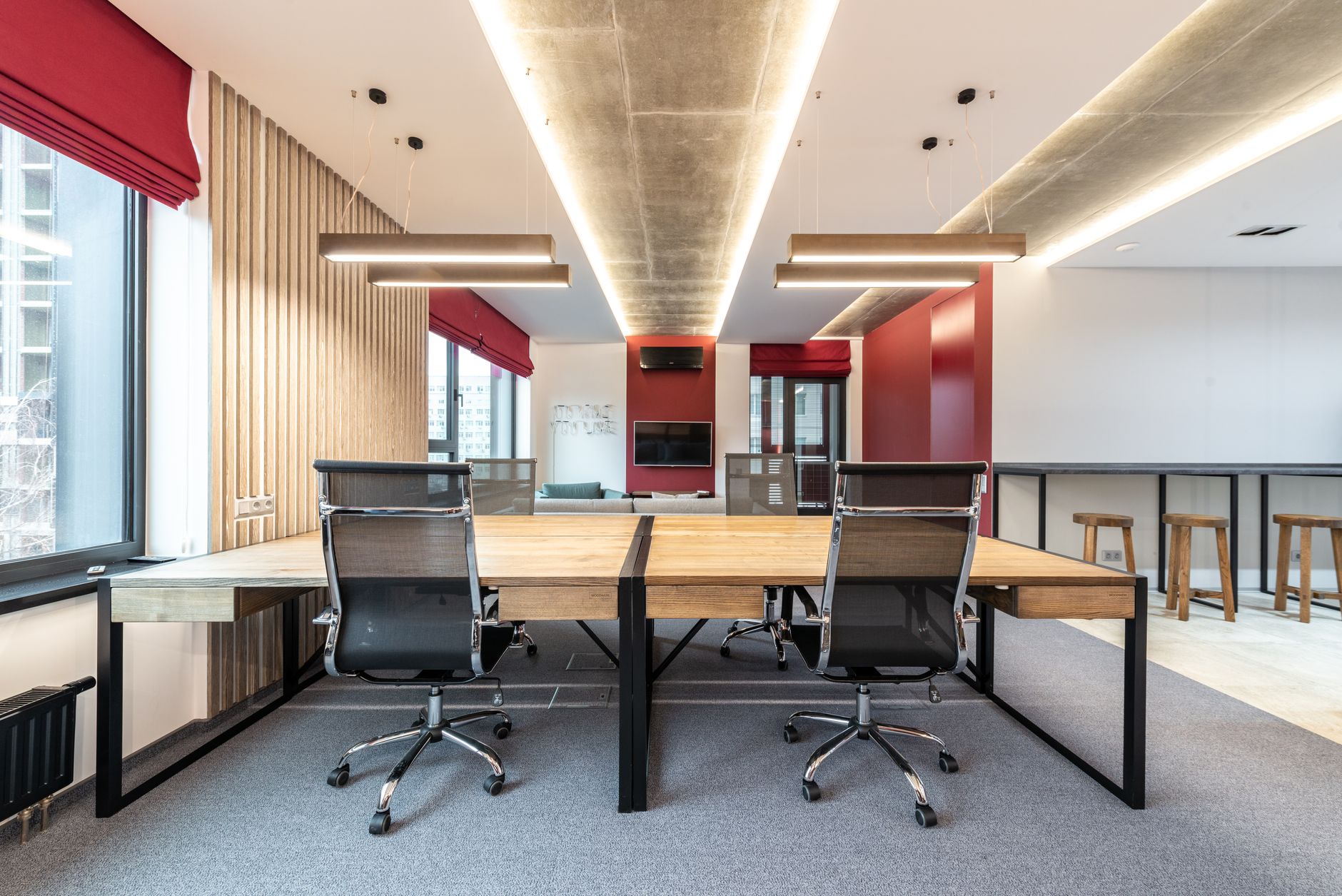 A modern open-plan startup office with wide monitors displaying video timeline editing interfaces, natural light streaming through floor-to-ceiling windows