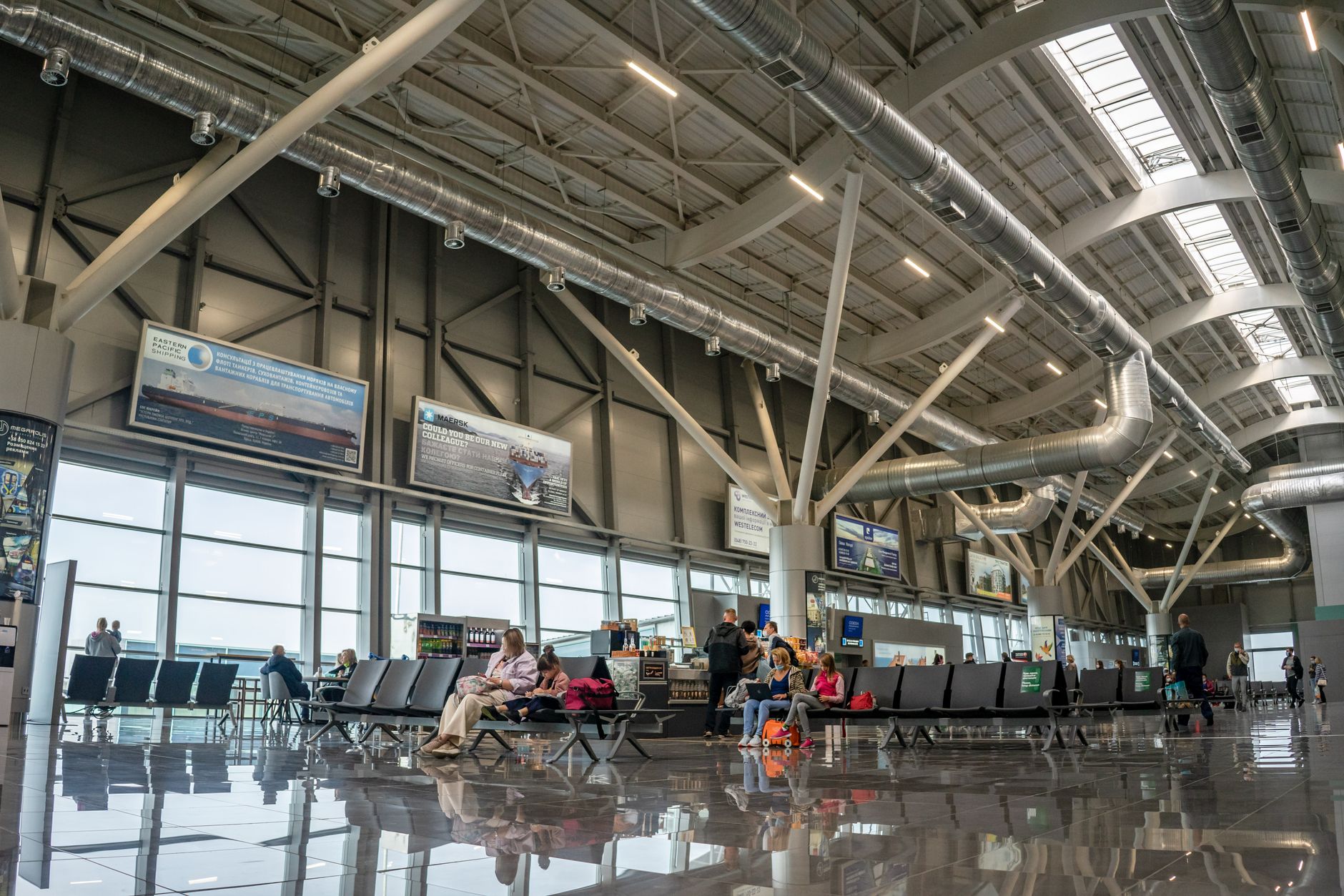 a departure terminal at a large international airport, wide shot showing empty gate seating, floor-to-ceiling windows overlooking a runway at dusk