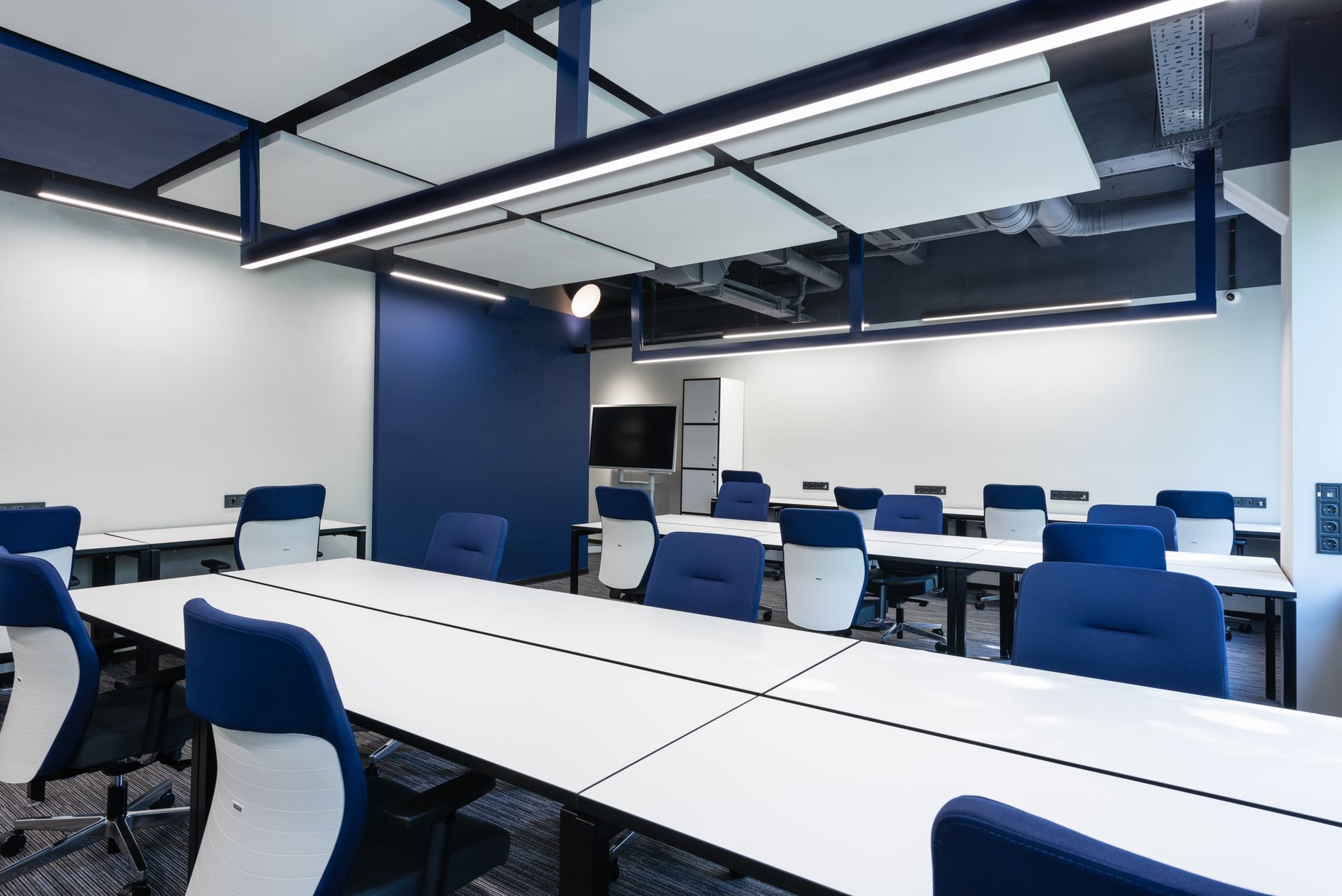 a modern open-plan office space with empty desks, monitors powered off, and server equipment stacked near the exit