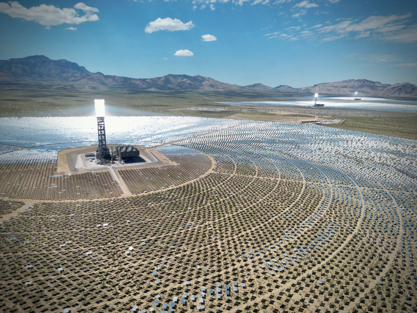 aerial view of a large data center campus under construction in an arid desert landscape, with solar panels visible along the perimeter
